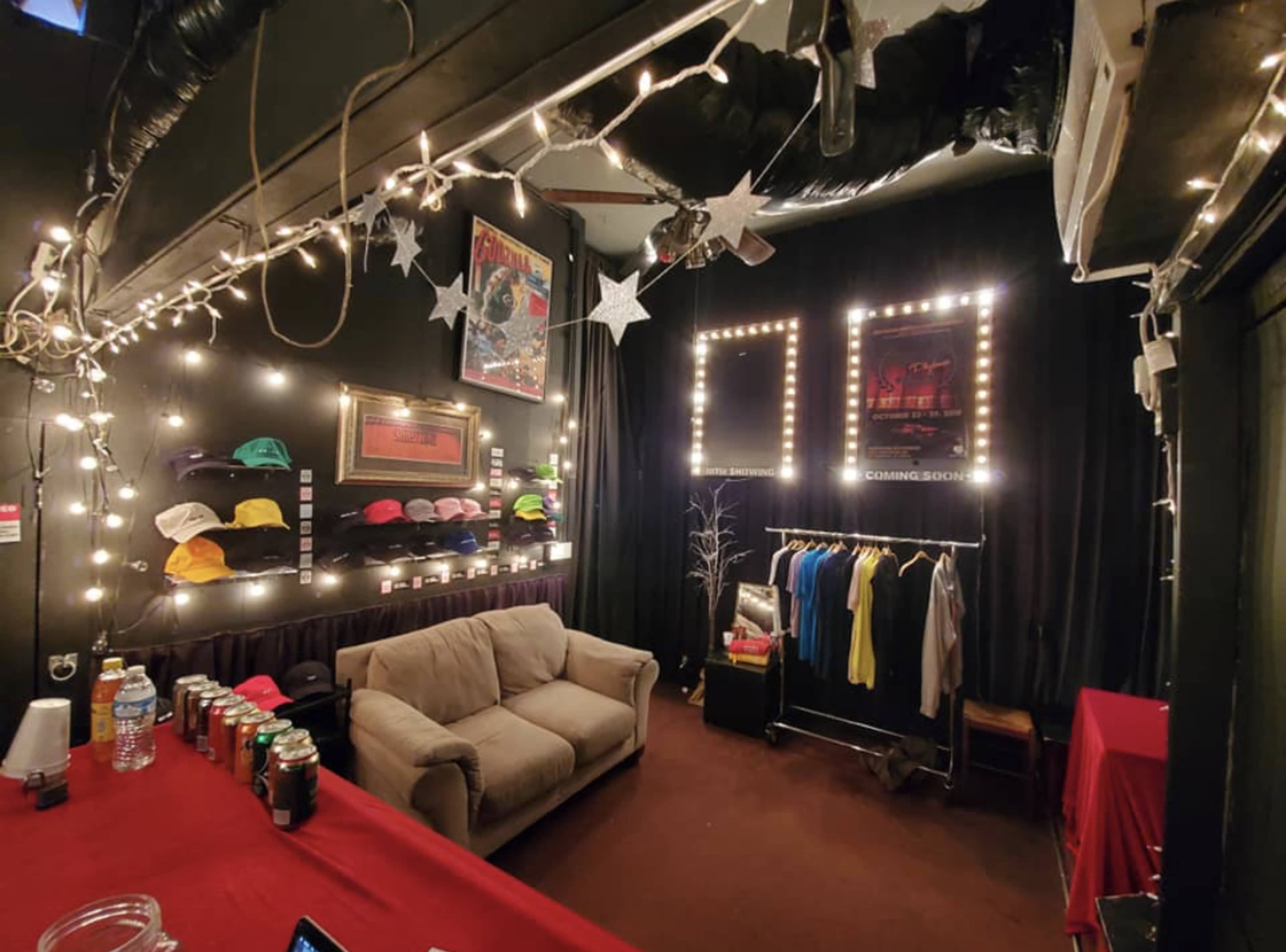 A small room decorated with string lights, featuring a couch, a rack of clothing, and a display of hats on the wall.