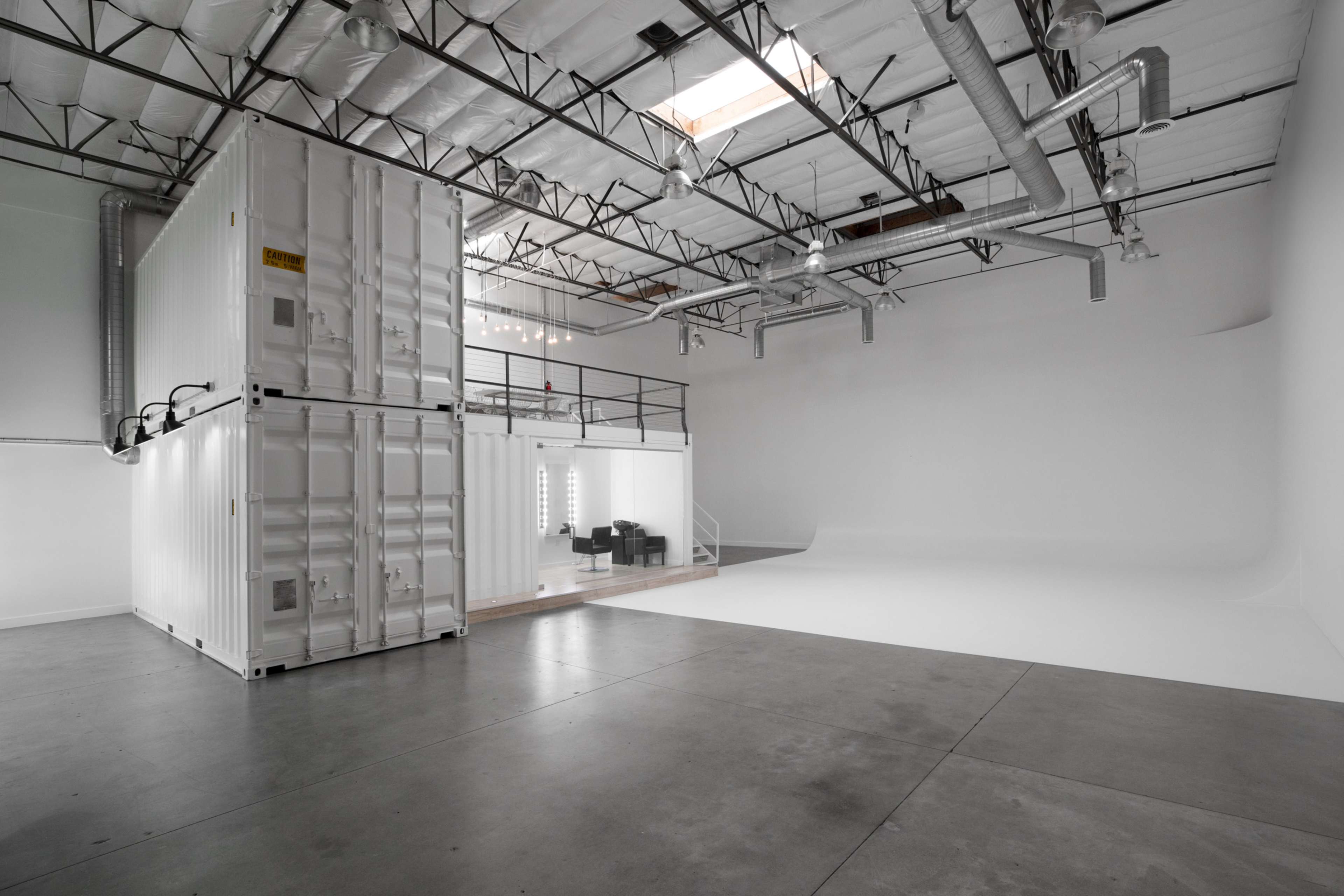 An empty studio space featuring two stacked shipping containers and a large white backdrop area.