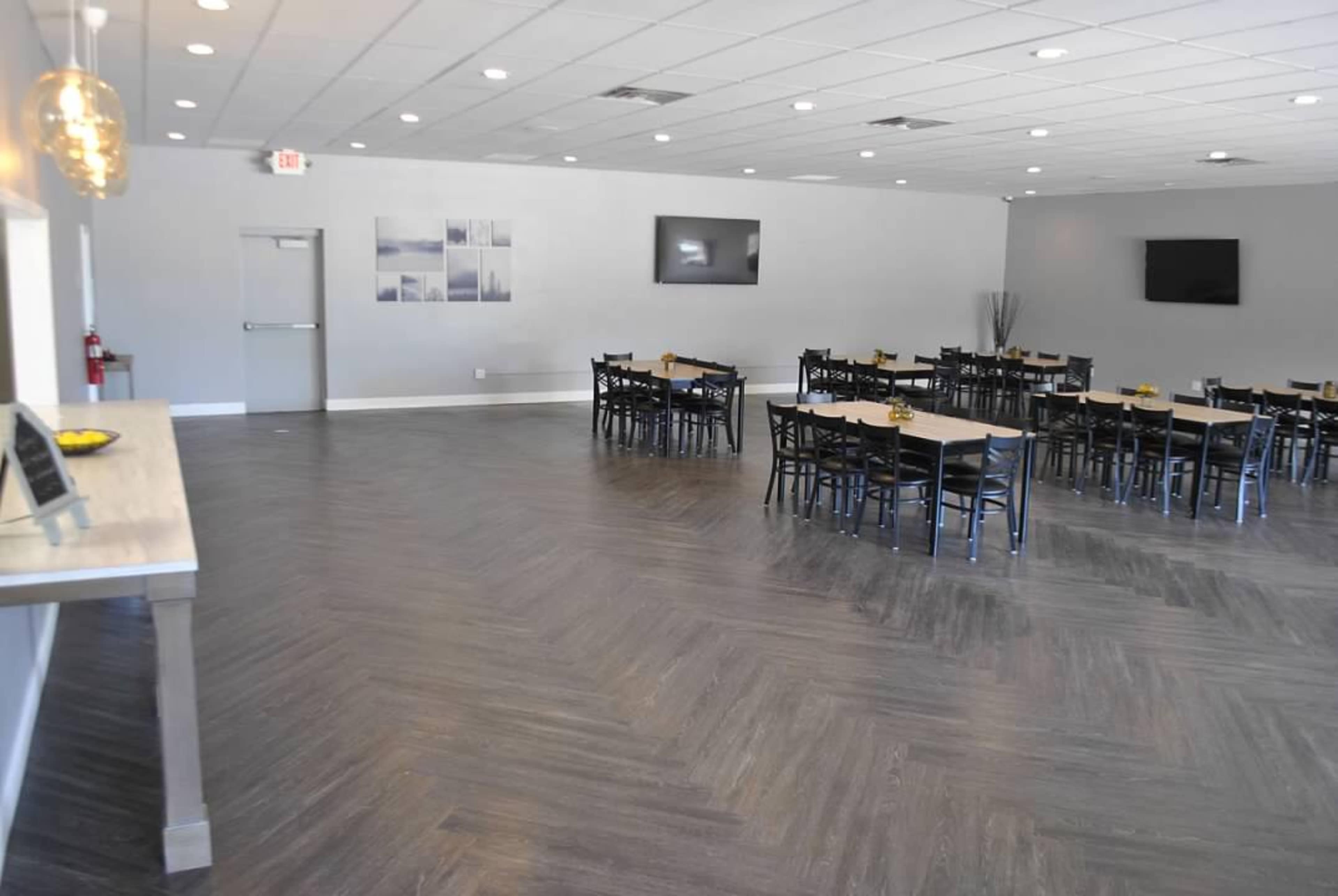 A spacious dining area with multiple tables and chairs, sleek decor, and two wall-mounted televisions.