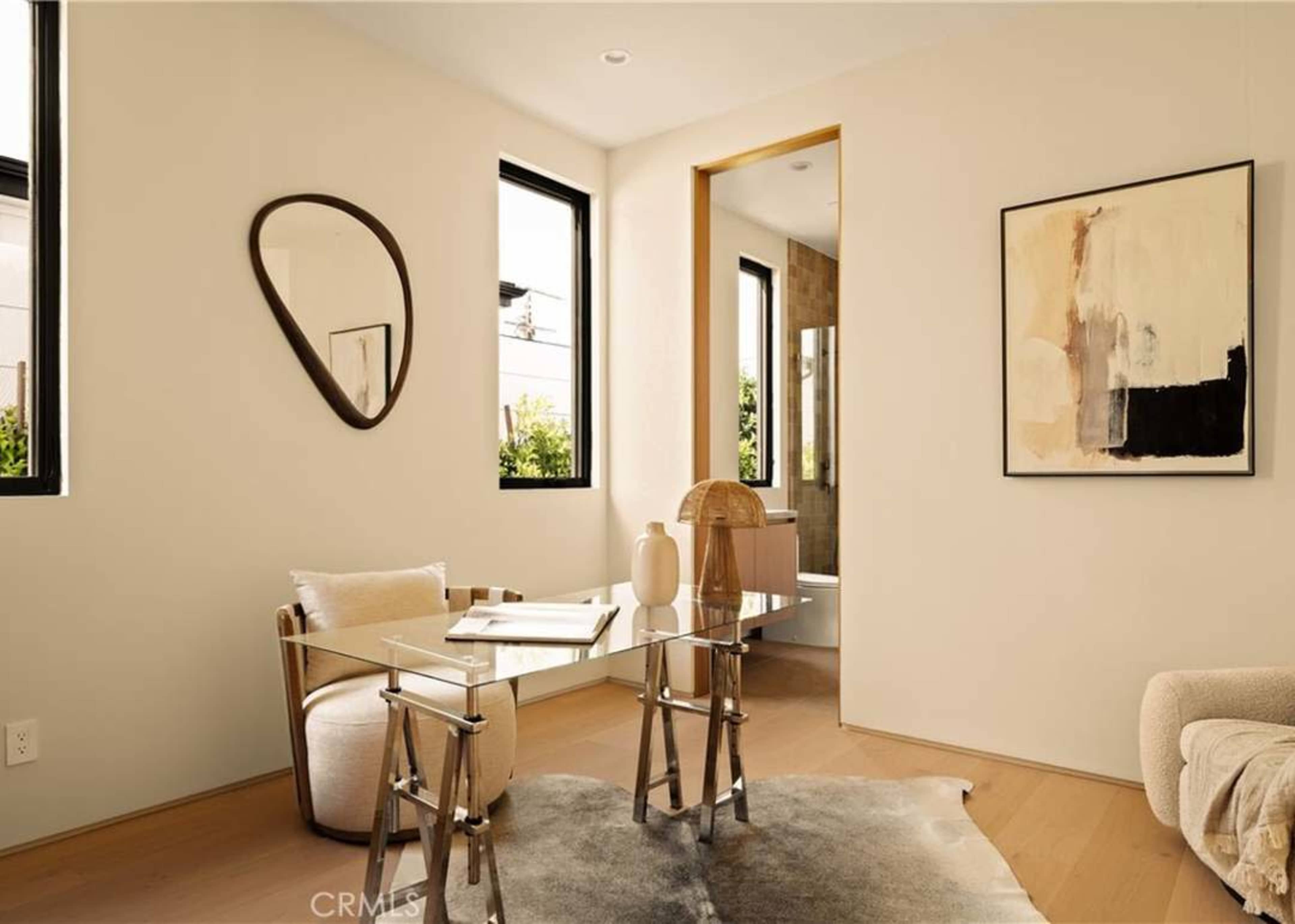 A modern, minimalist workspace features a glass desk, a stylish chair, and a large window allowing natural light.