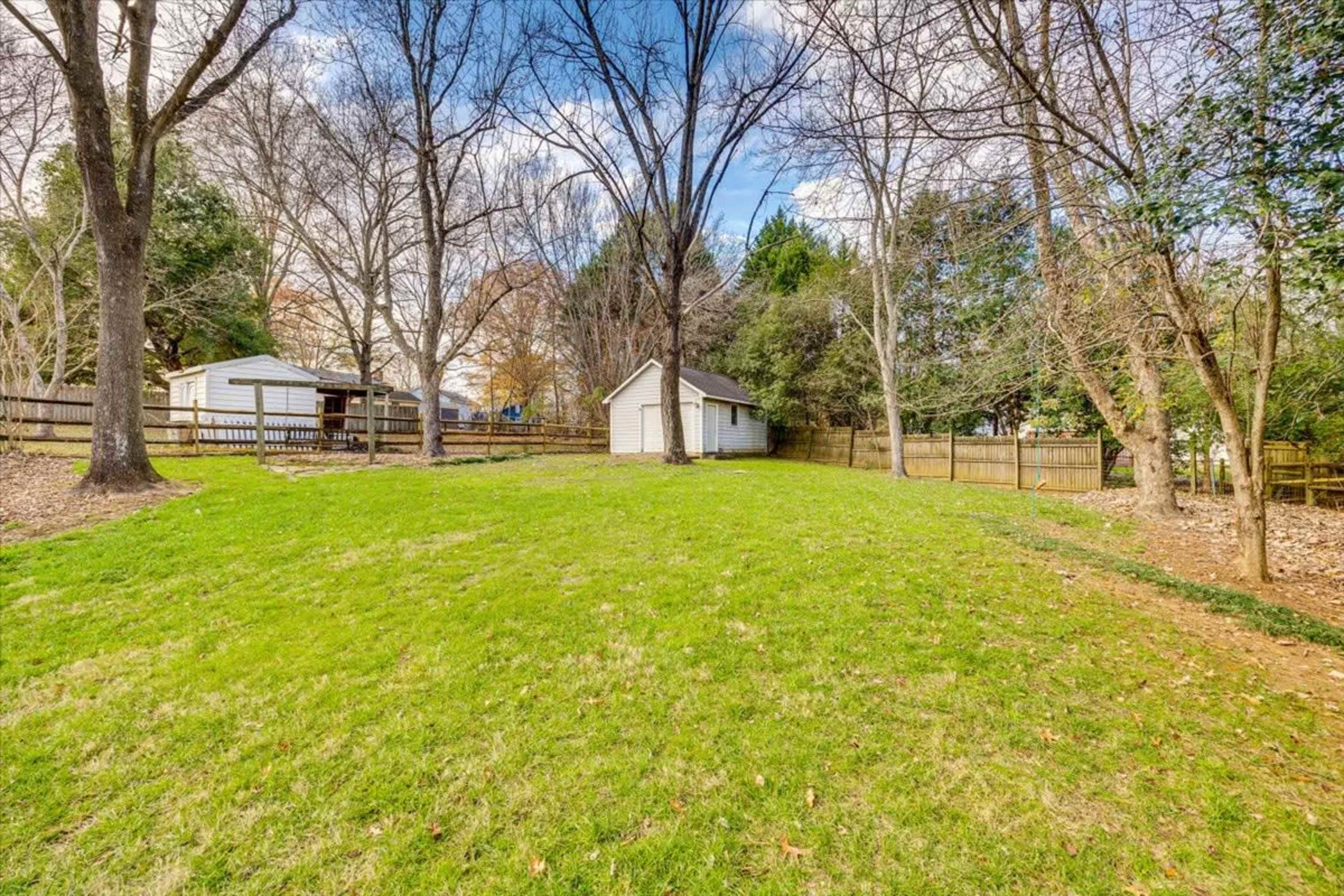 The image shows a grassy backyard with a small white shed and several trees in a residential setting.