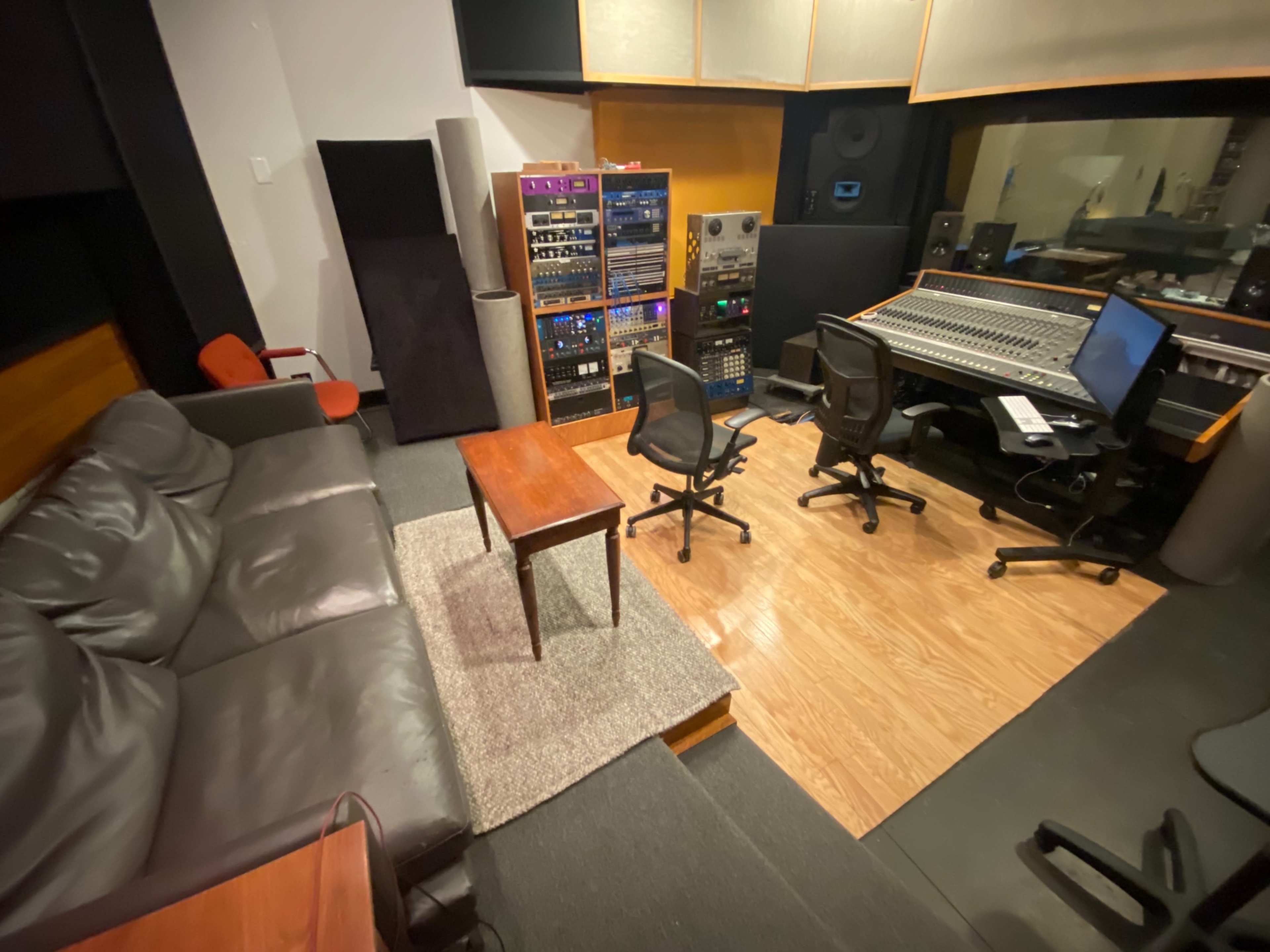 A recording studio with a mixing console, audio equipment, and a small seating area featuring a sofa and coffee table.