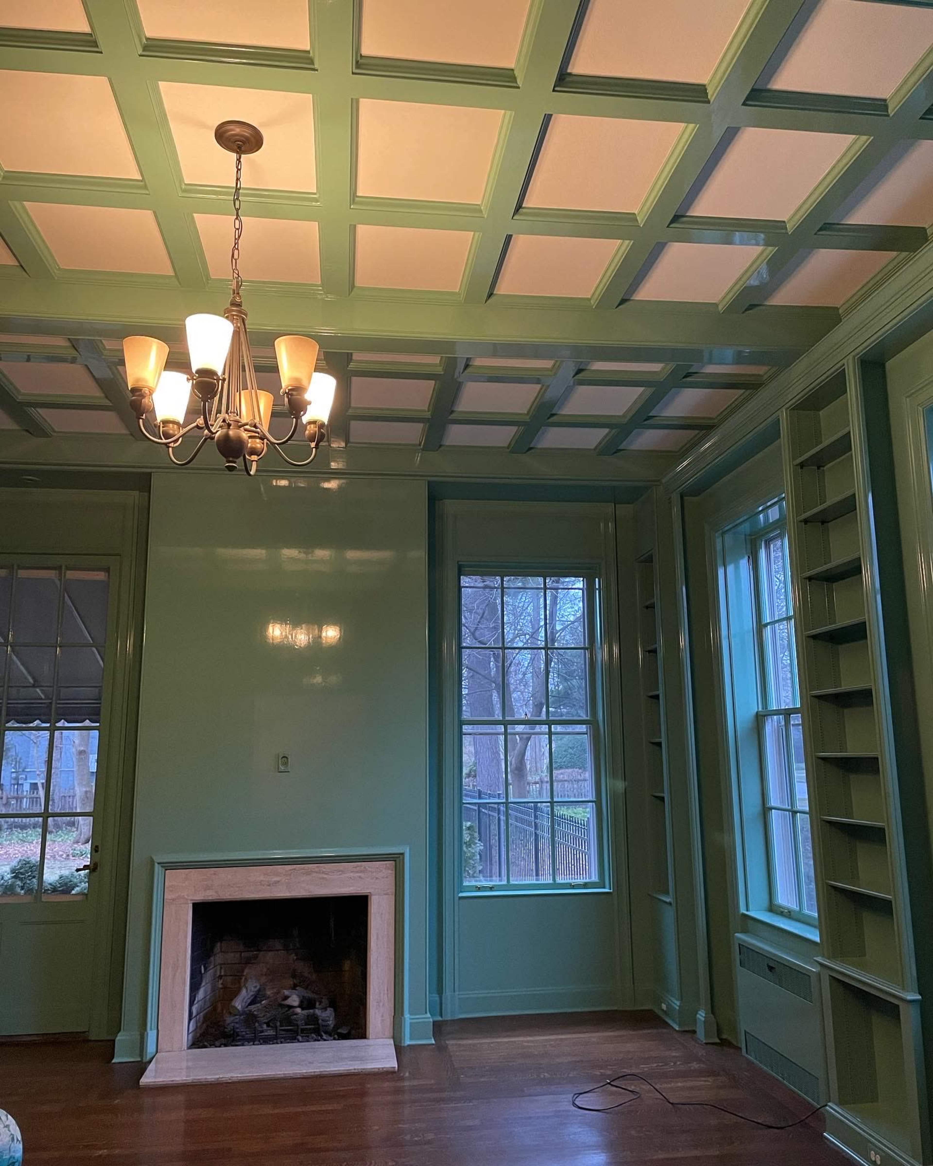 The image shows a room with green walls, a coffered ceiling, a chandelier, and a fireplace with a marble surround.