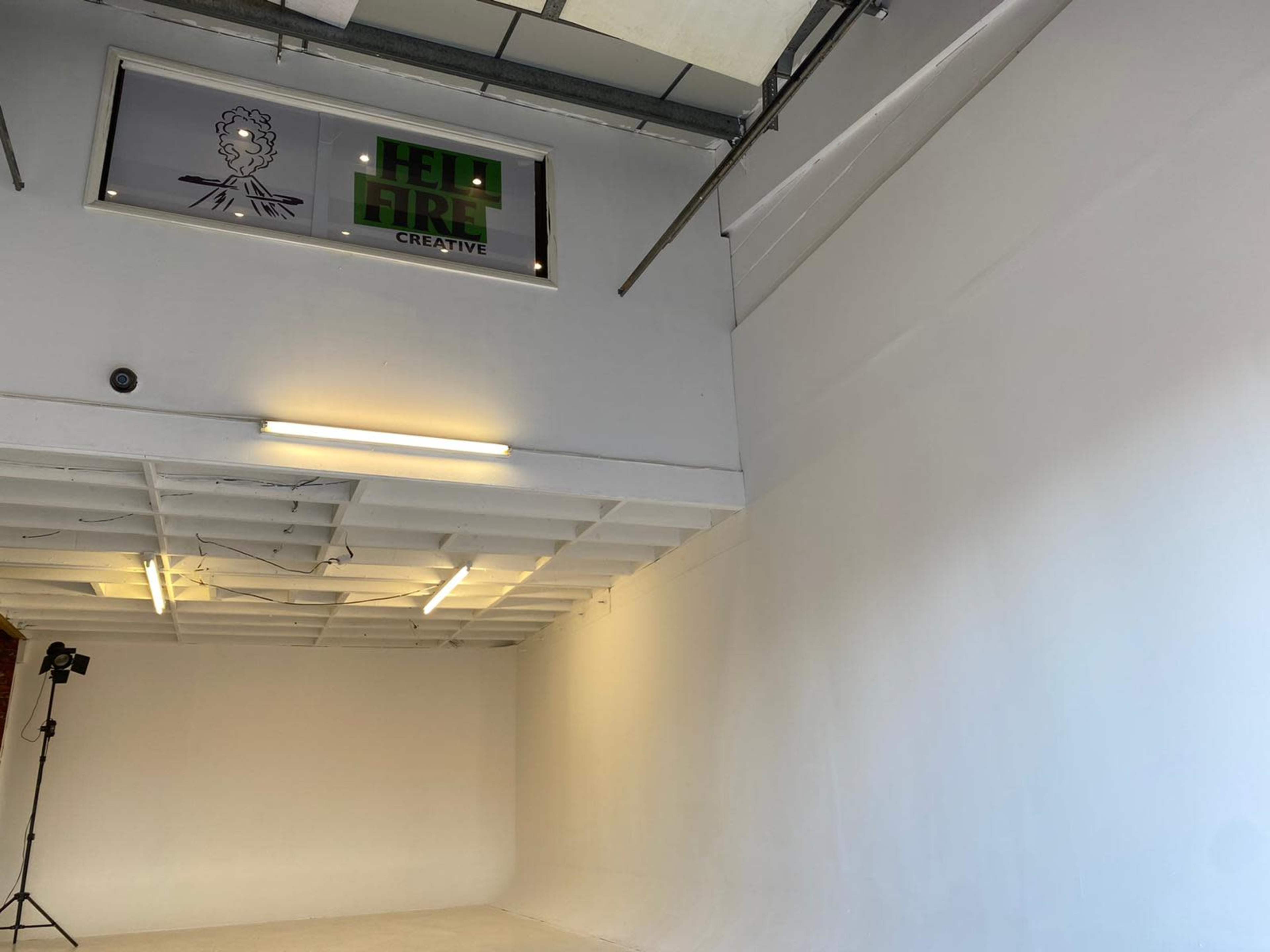 A spacious, well-lit studio with white walls, a small sign reading "FELT FIRE CREATIVE," and a single spotlight setup in the corner.