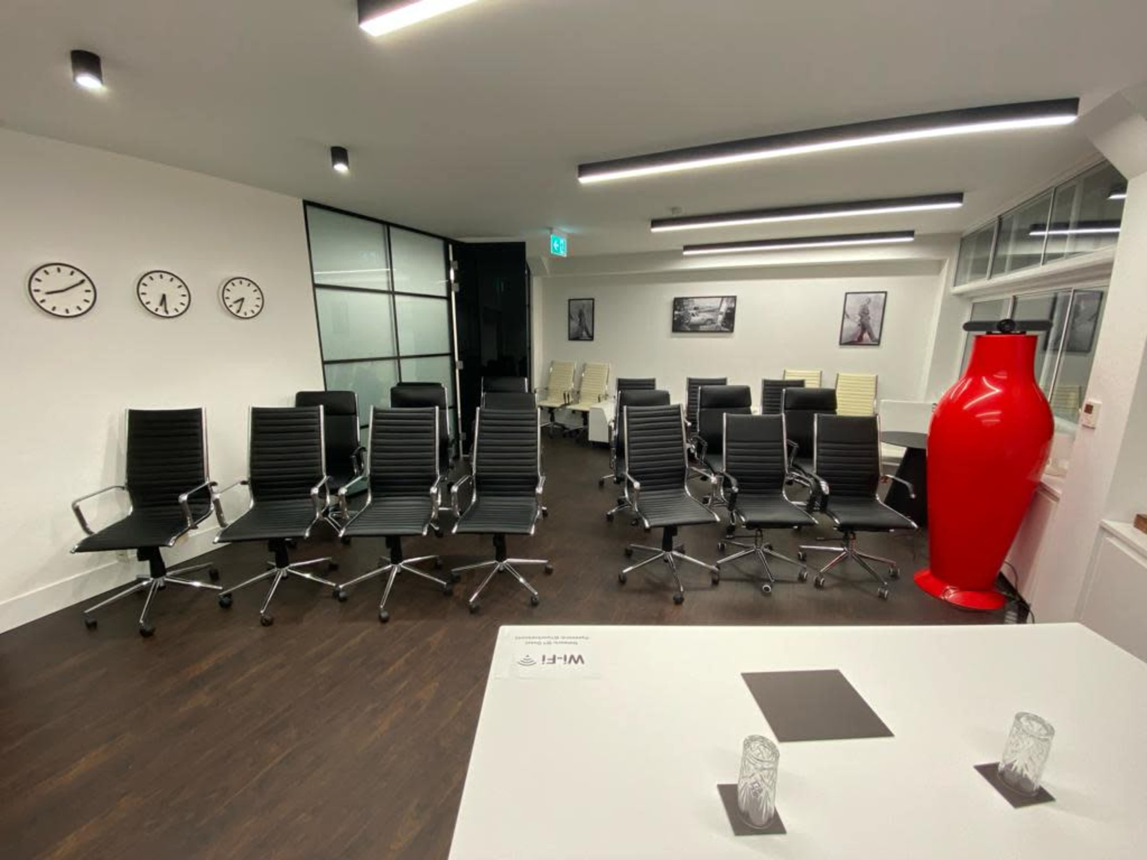 A modern conference room with black rolling chairs arranged in rows and a large red vase in the corner.