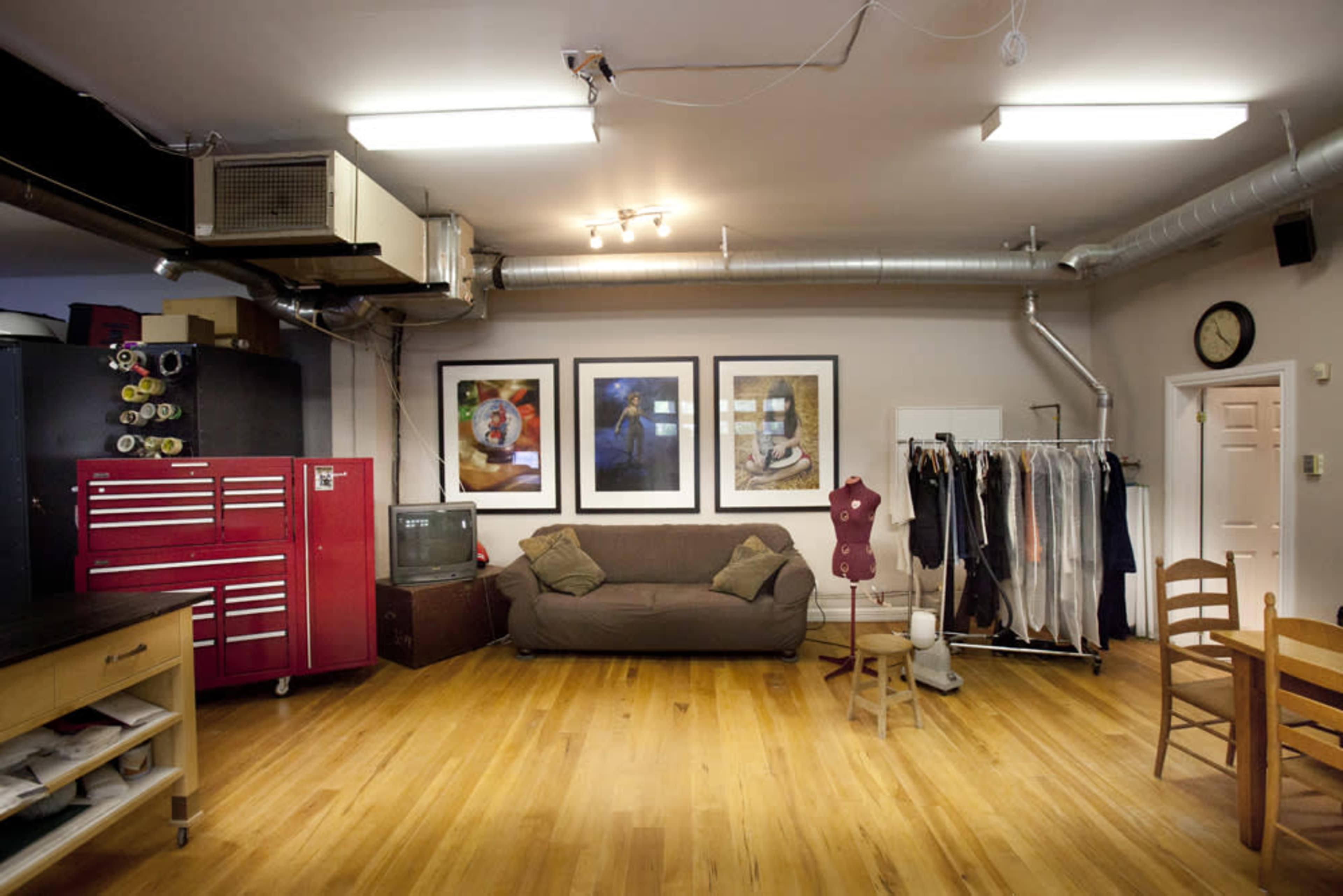 A studio space featuring a couch, a clothing rack, framed artwork on the walls, and a red tool cabinet.