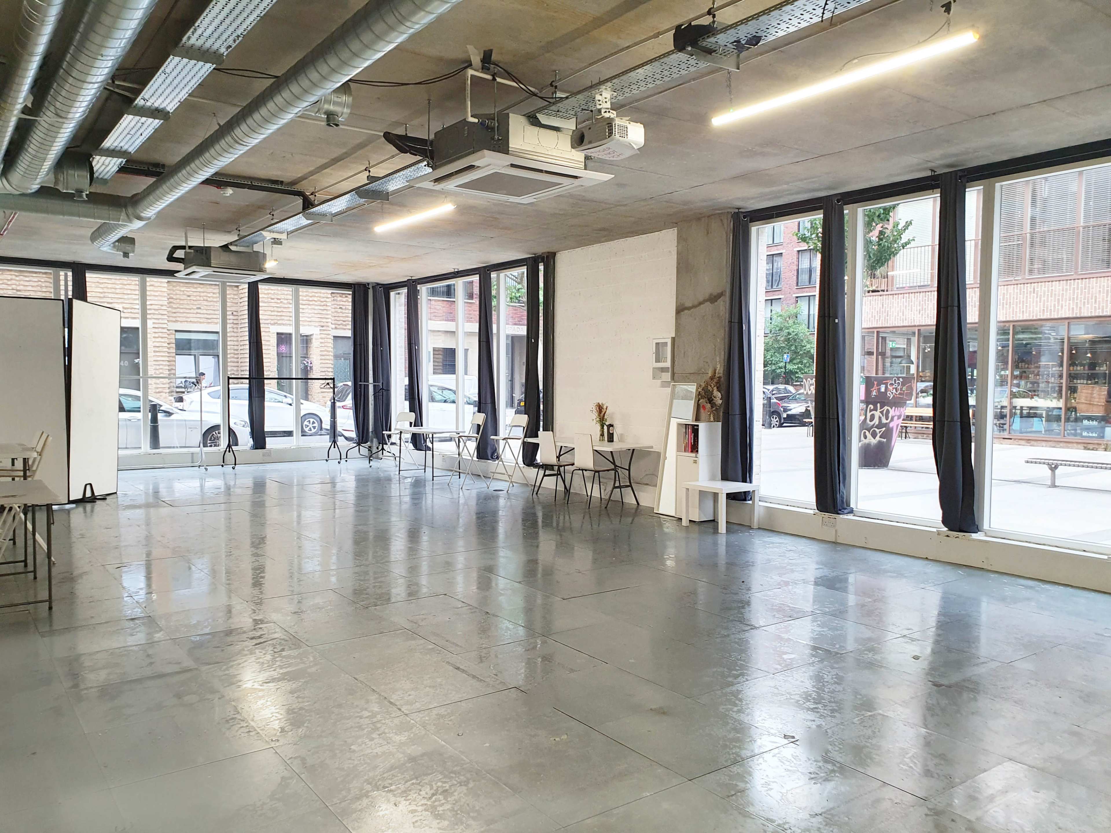 A spacious, minimalist interior with polished concrete flooring, large windows, and a few tables and chairs arranged in an open area.