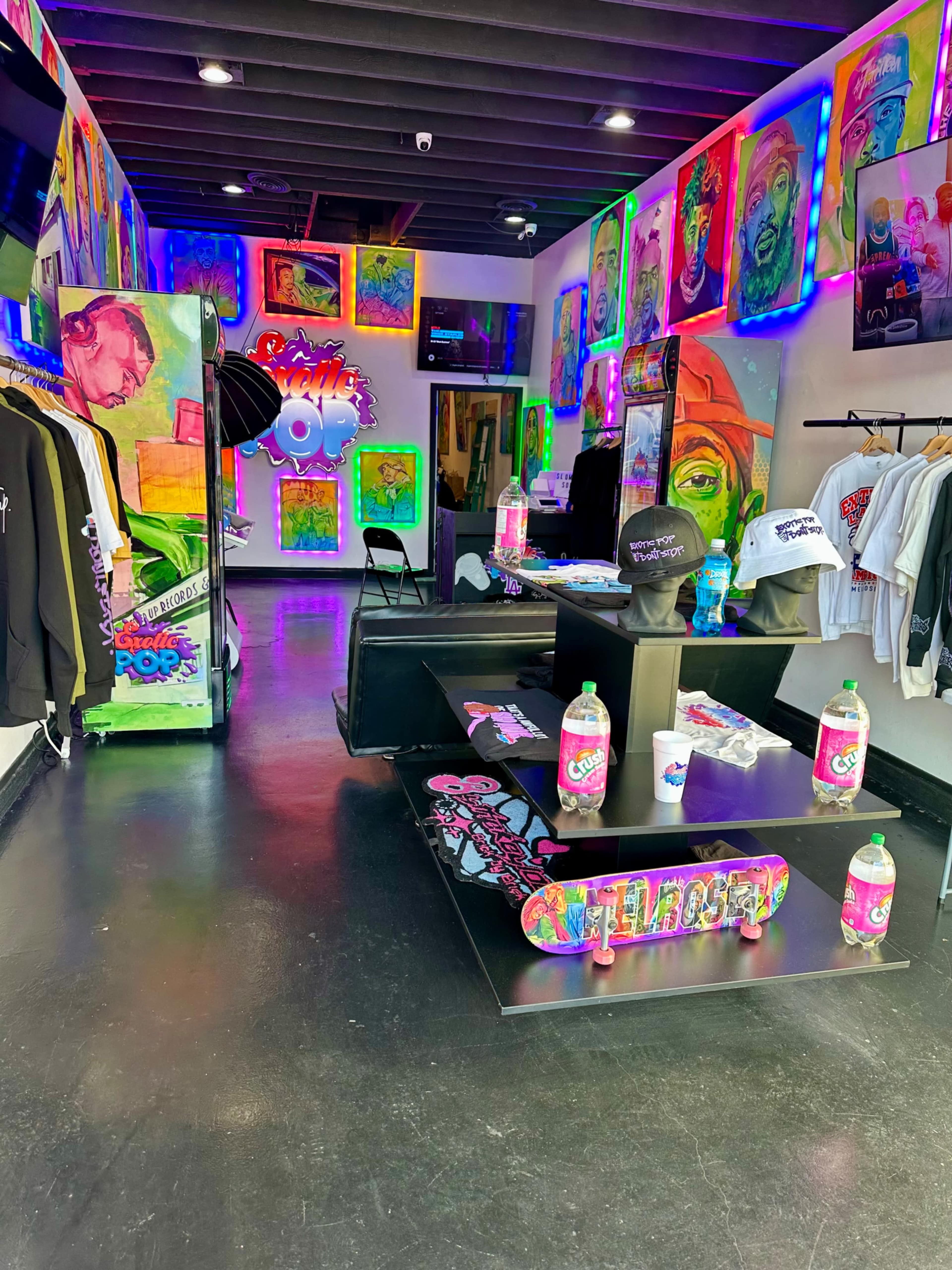 The image shows a vibrant retail space featuring colorful artwork on the walls, skateboards displayed on a table, and various clothing items hanging nearby.