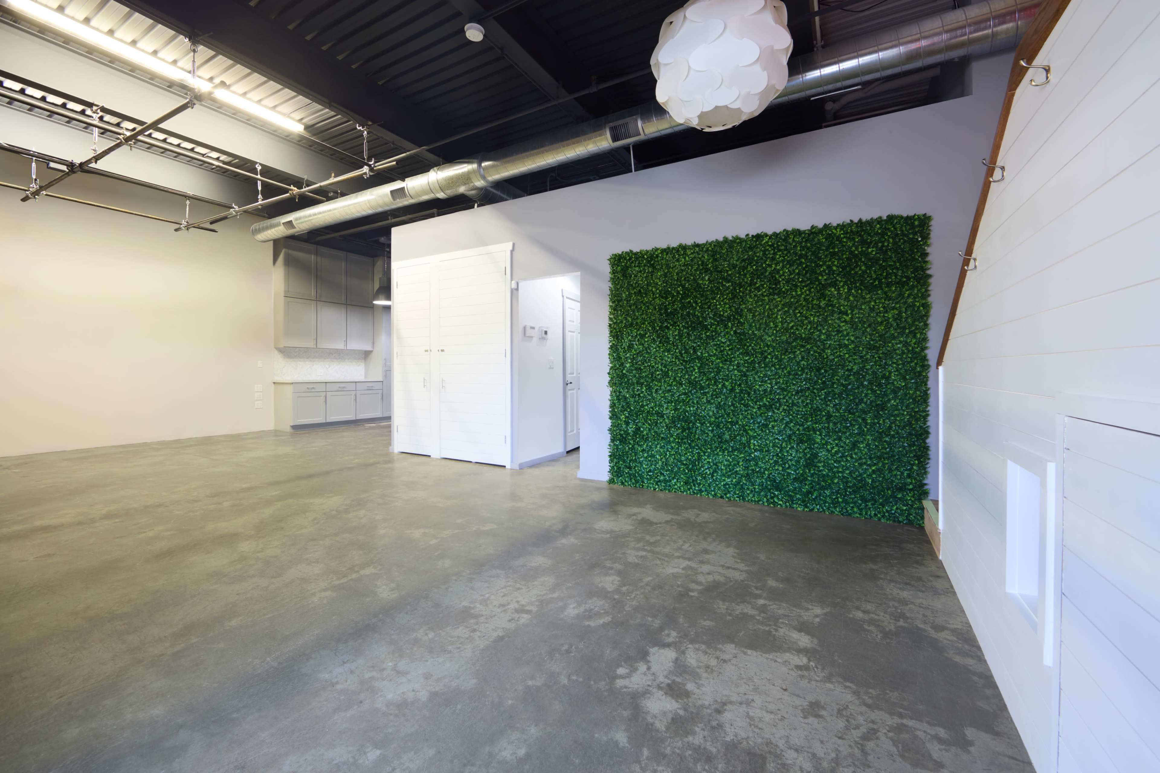 The image shows a spacious, modern interior with polished concrete flooring, a green wall covered in artificial leaves, and white storage units.