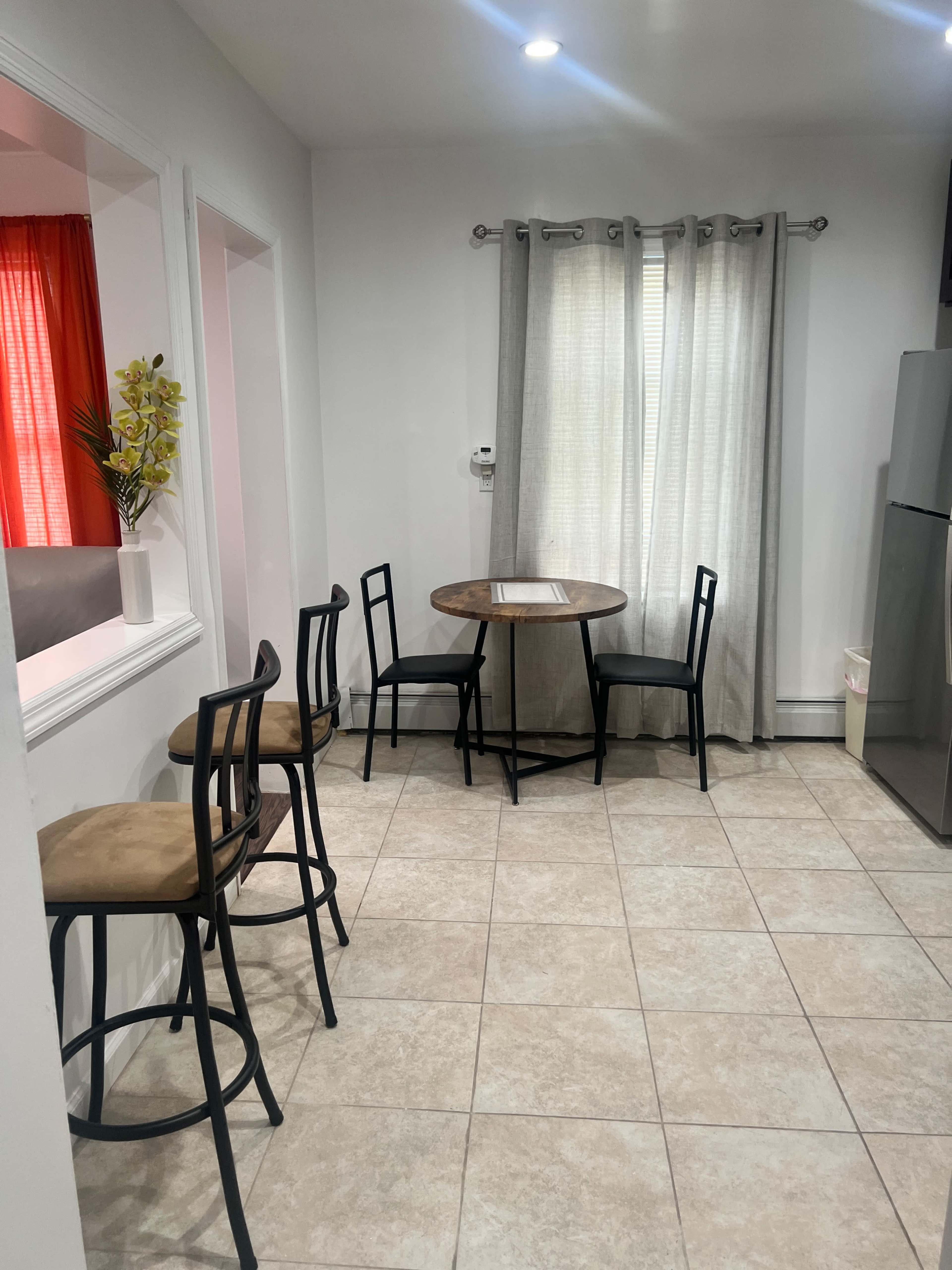 A small dining area with a round table and four chairs near a wall with a window covered by curtains.