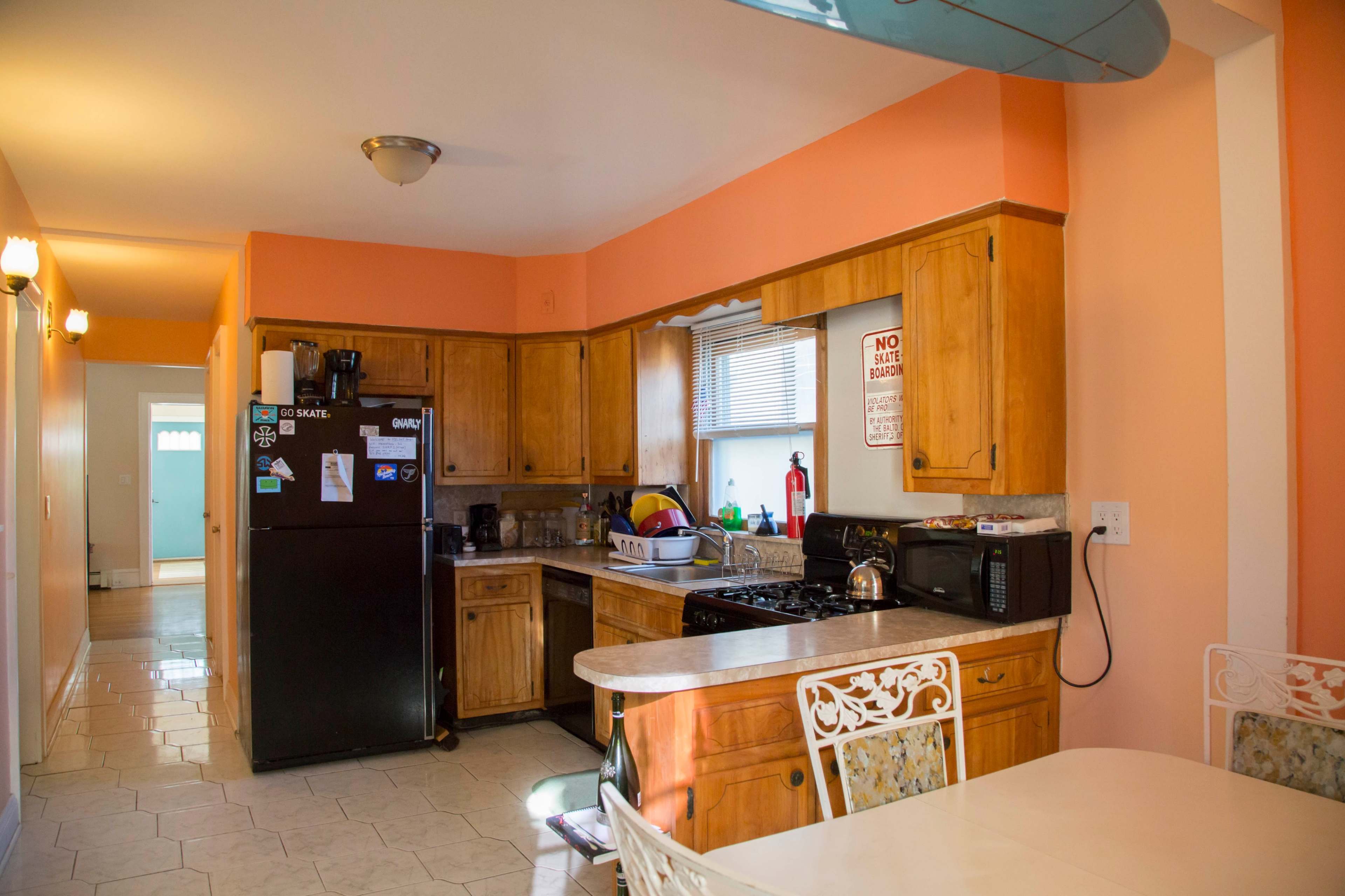 A kitchen with wooden cabinets, a black refrigerator, and a table with white chairs, all set against a peach-colored wall.