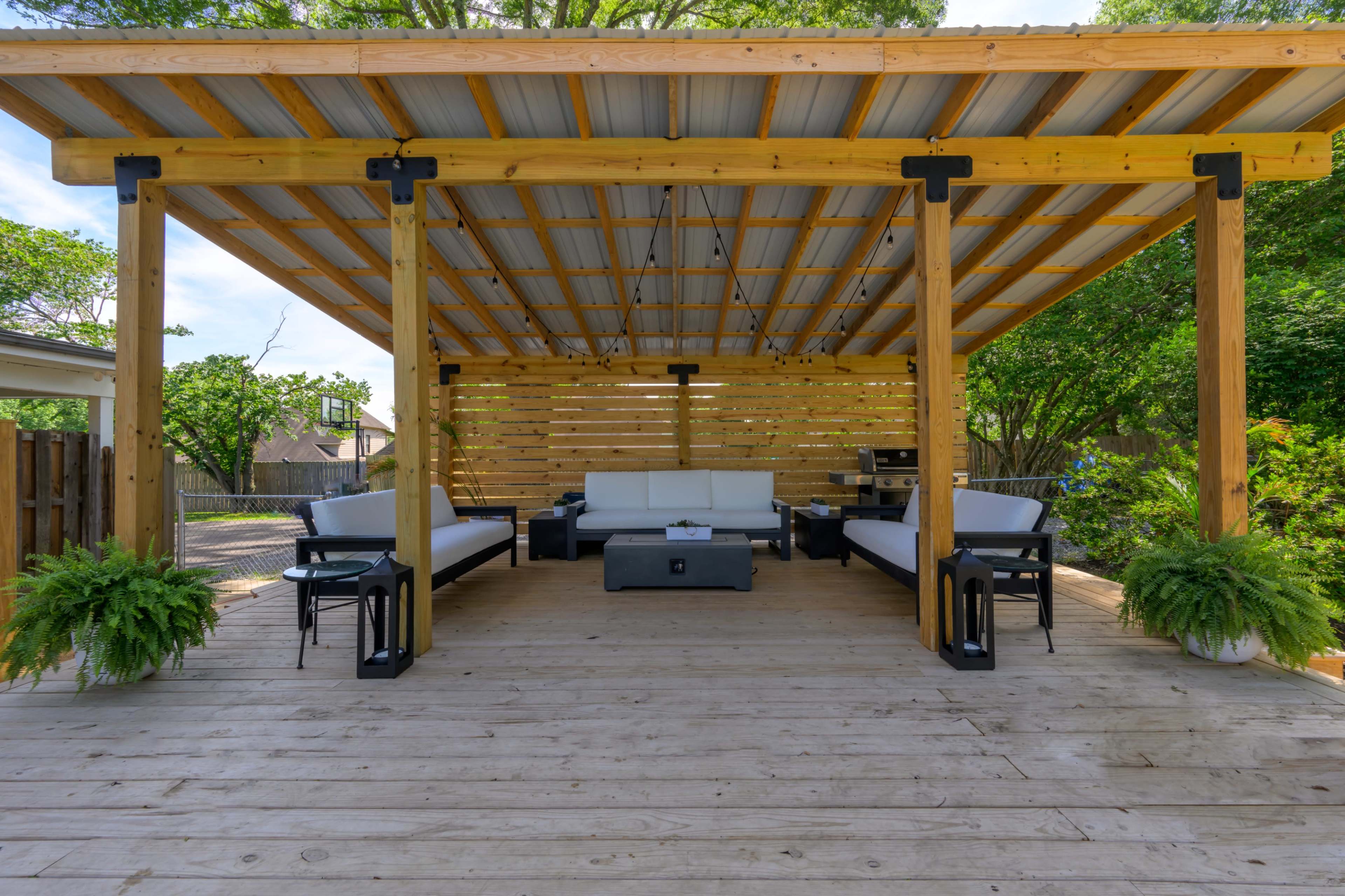 A wooden deck features a covered seating area with a sofa set, coffee table, and planters.