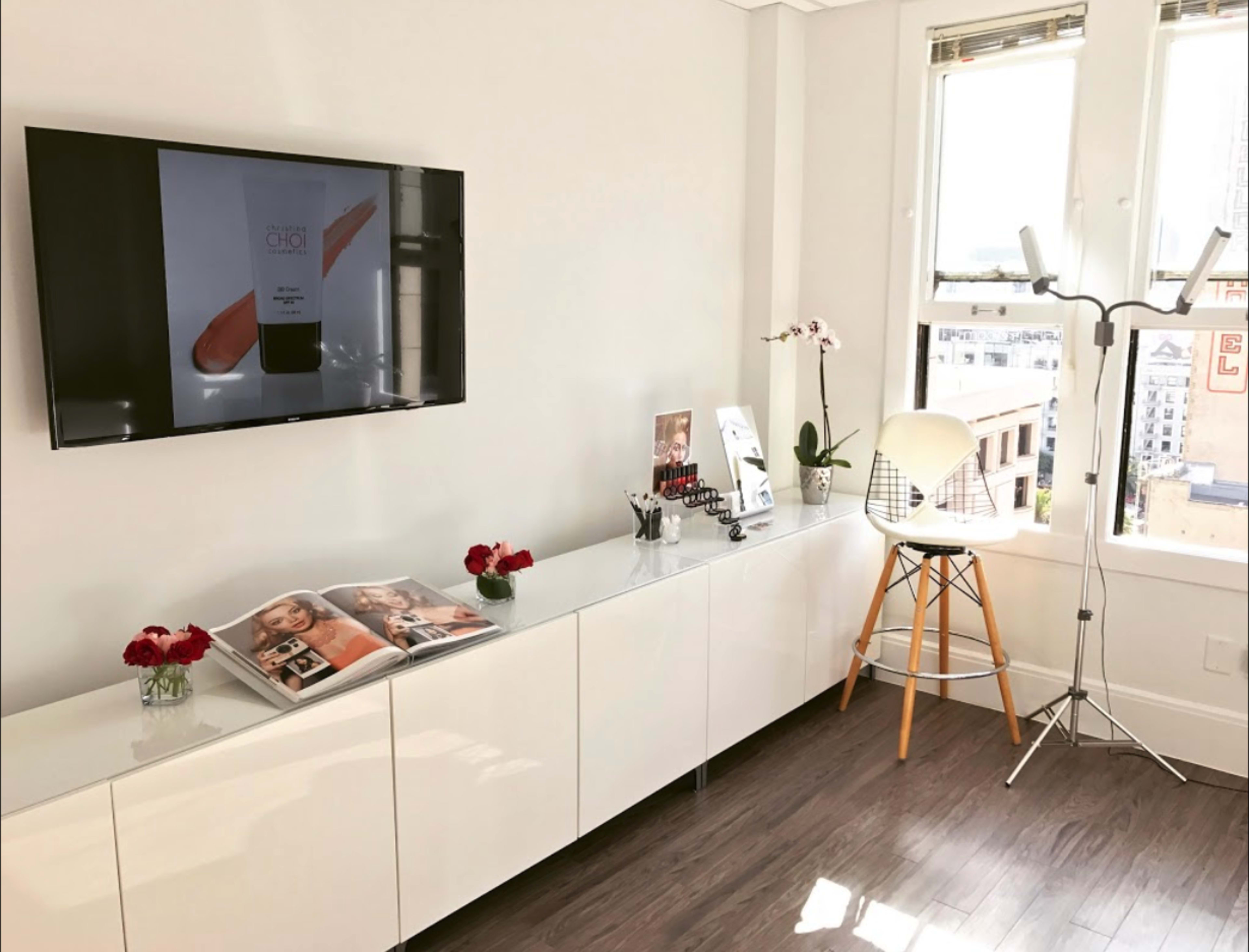 A modern salon interior featuring a wall-mounted television, a stylish white cabinet with decorative items, and a bar stool beside a floor lamp.
