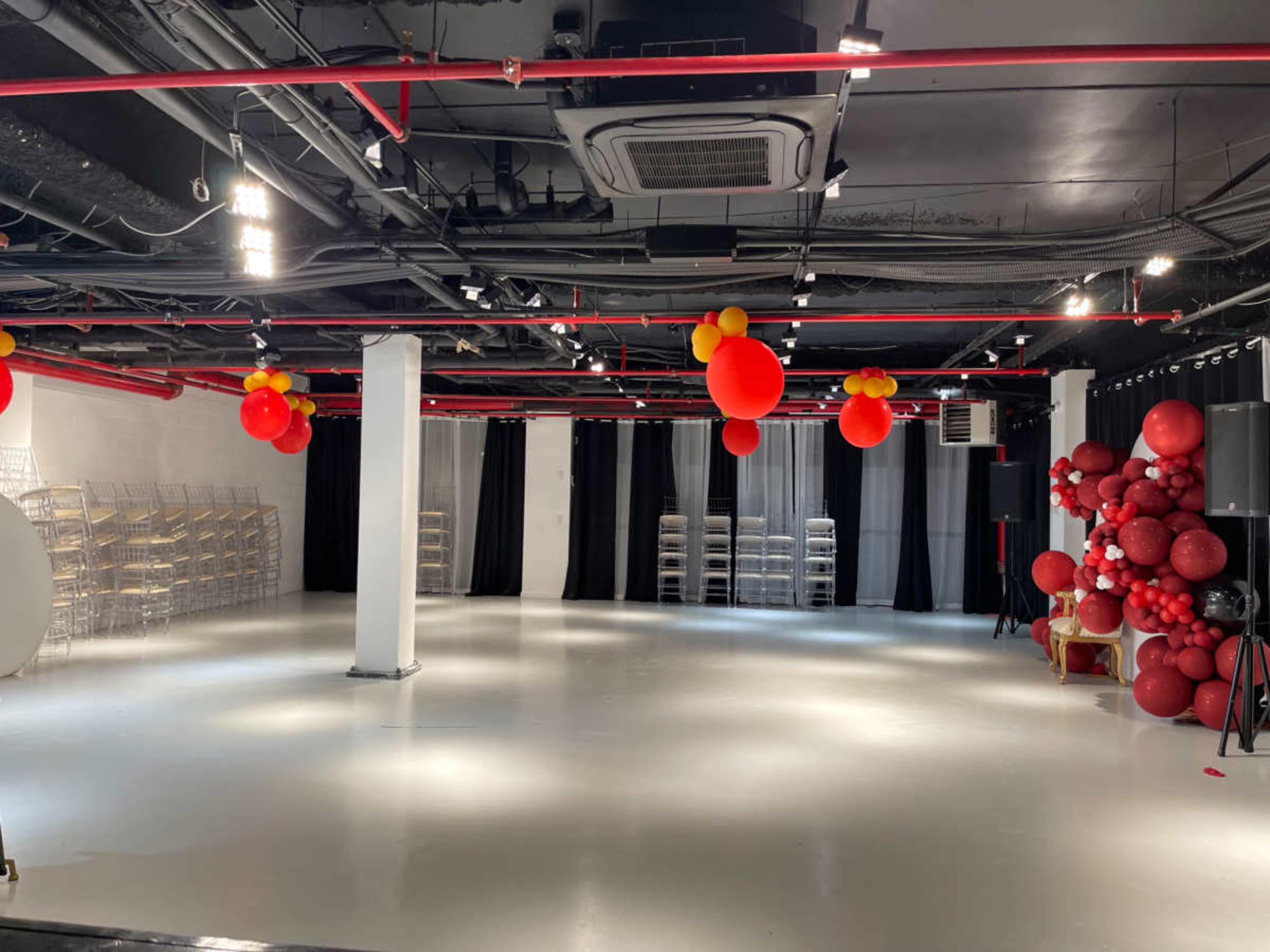 A spacious, empty room with white floors, black curtains, and decorative red and yellow balloons scattered throughout.