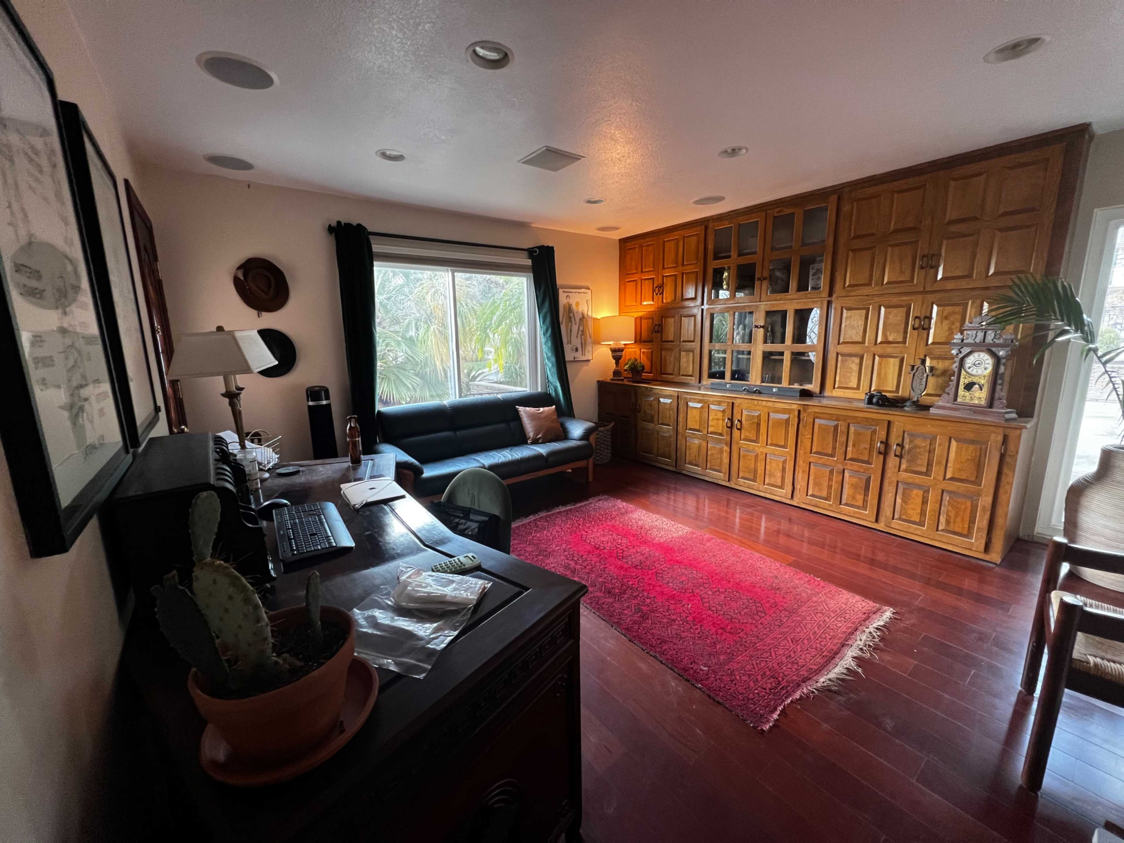 A modern living room with a dark leather sofa, a wooden cabinet, and a desk with a computer, all arranged on polished wooden flooring.