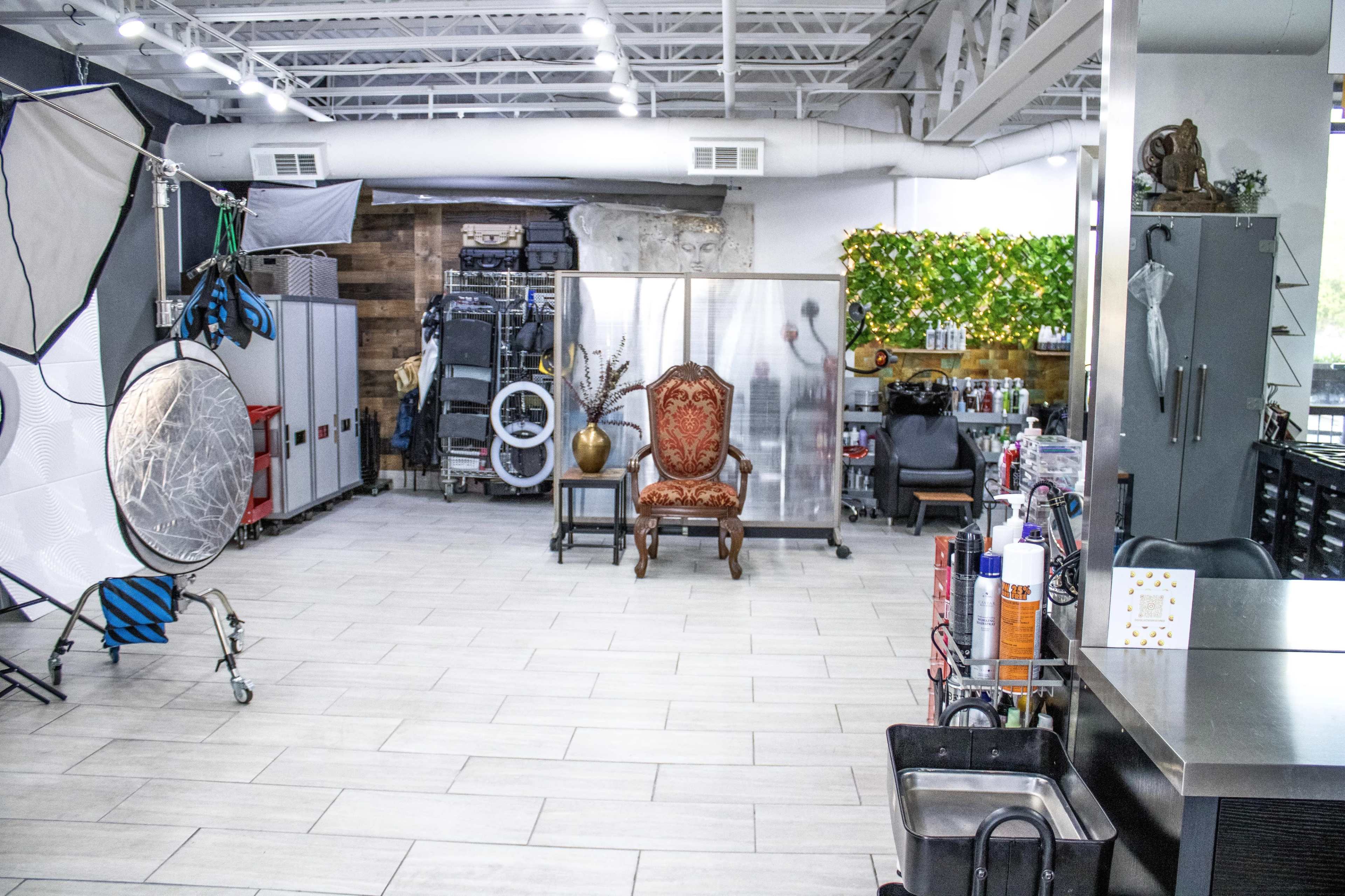 A spacious studio with various photography equipment, including a large reflector, and a vintage chair positioned in the center, surrounded by shelves and storage units.