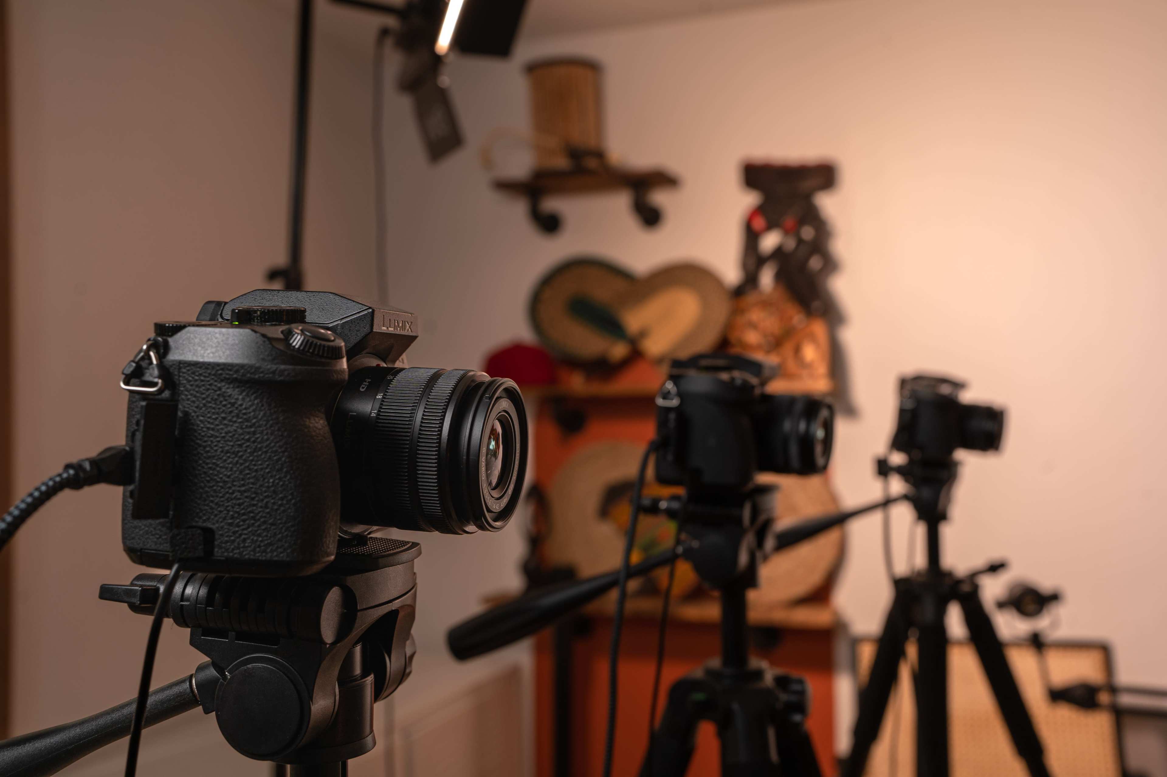 Three cameras mounted on tripods in a room adorned with decorative items on the wall.