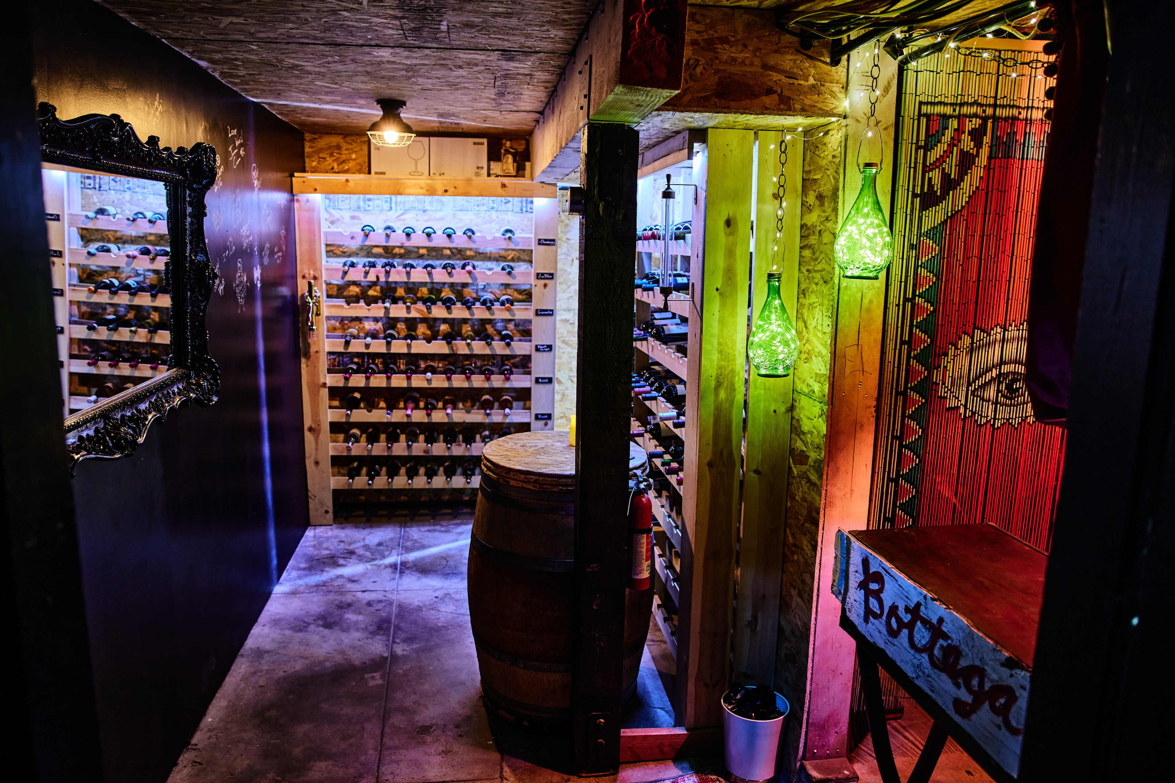 A dimly lit wine cellar with wooden shelves filled with bottles, a barrel, and decorative lighting.