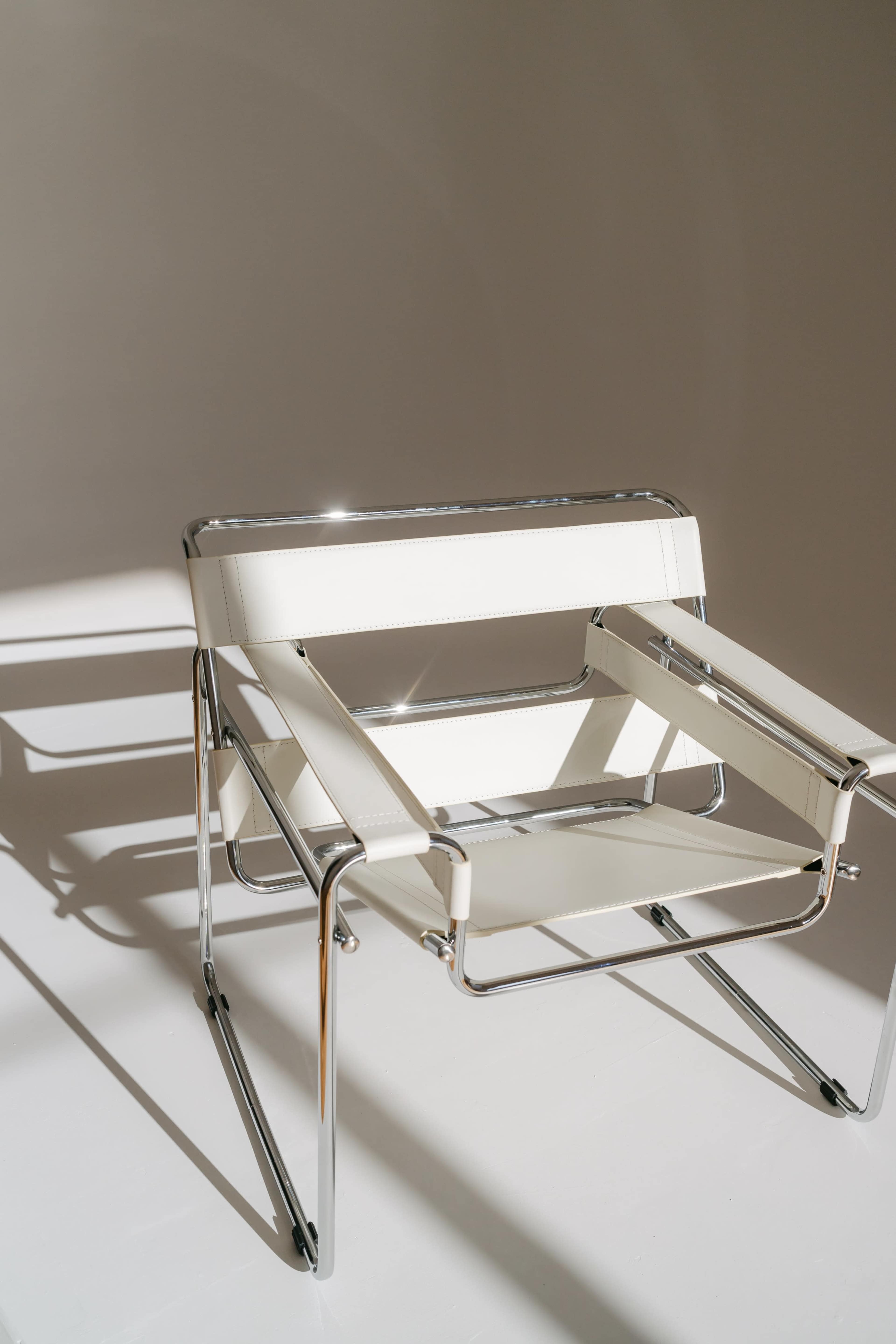 A modern white chair with a chrome frame is positioned against a neutral backdrop, casting distinct shadows on the surface below.