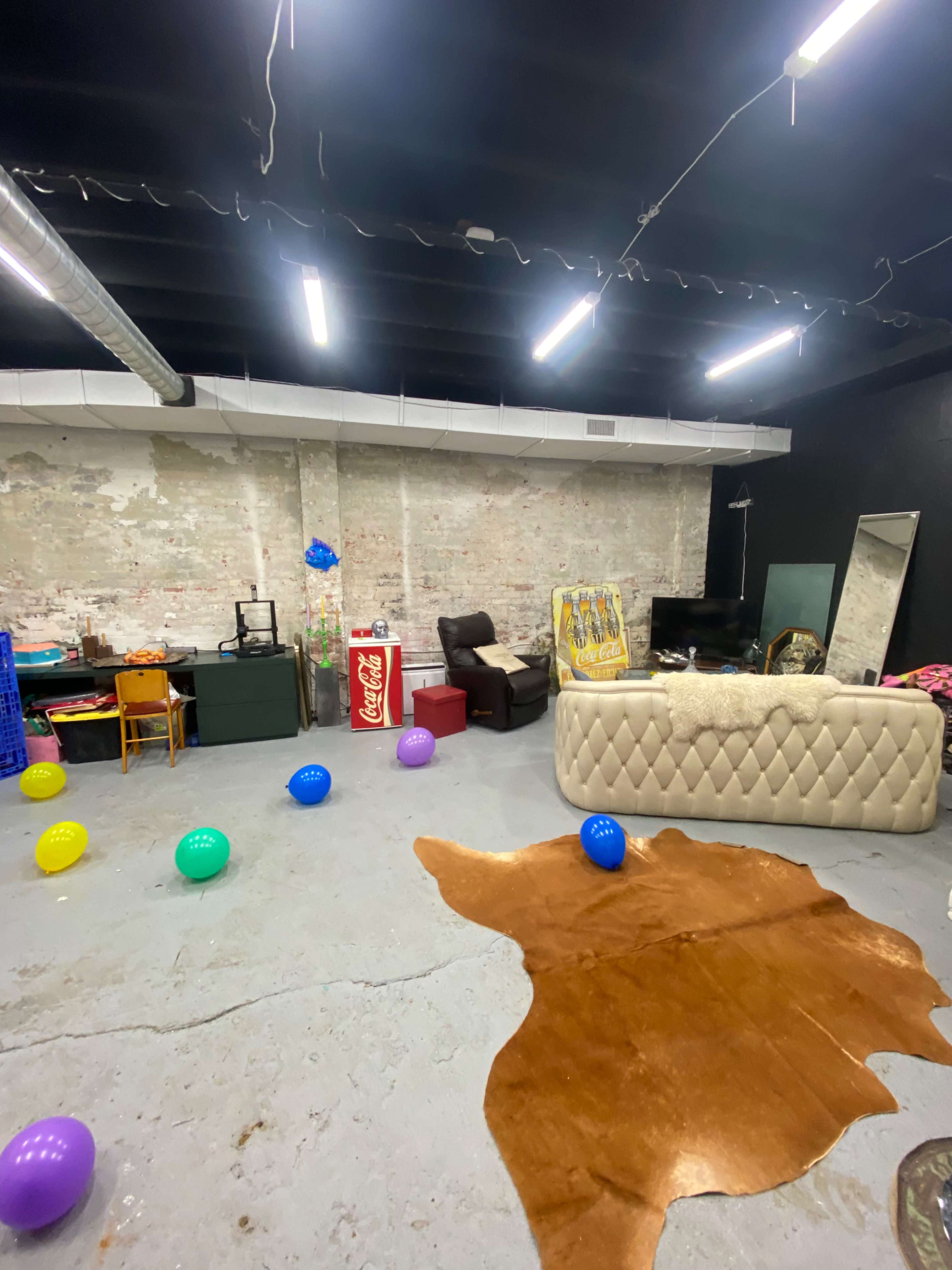 The room features a textured concrete floor, a large sofa, a mirror, a television, and scattered colorful balloons on the ground.