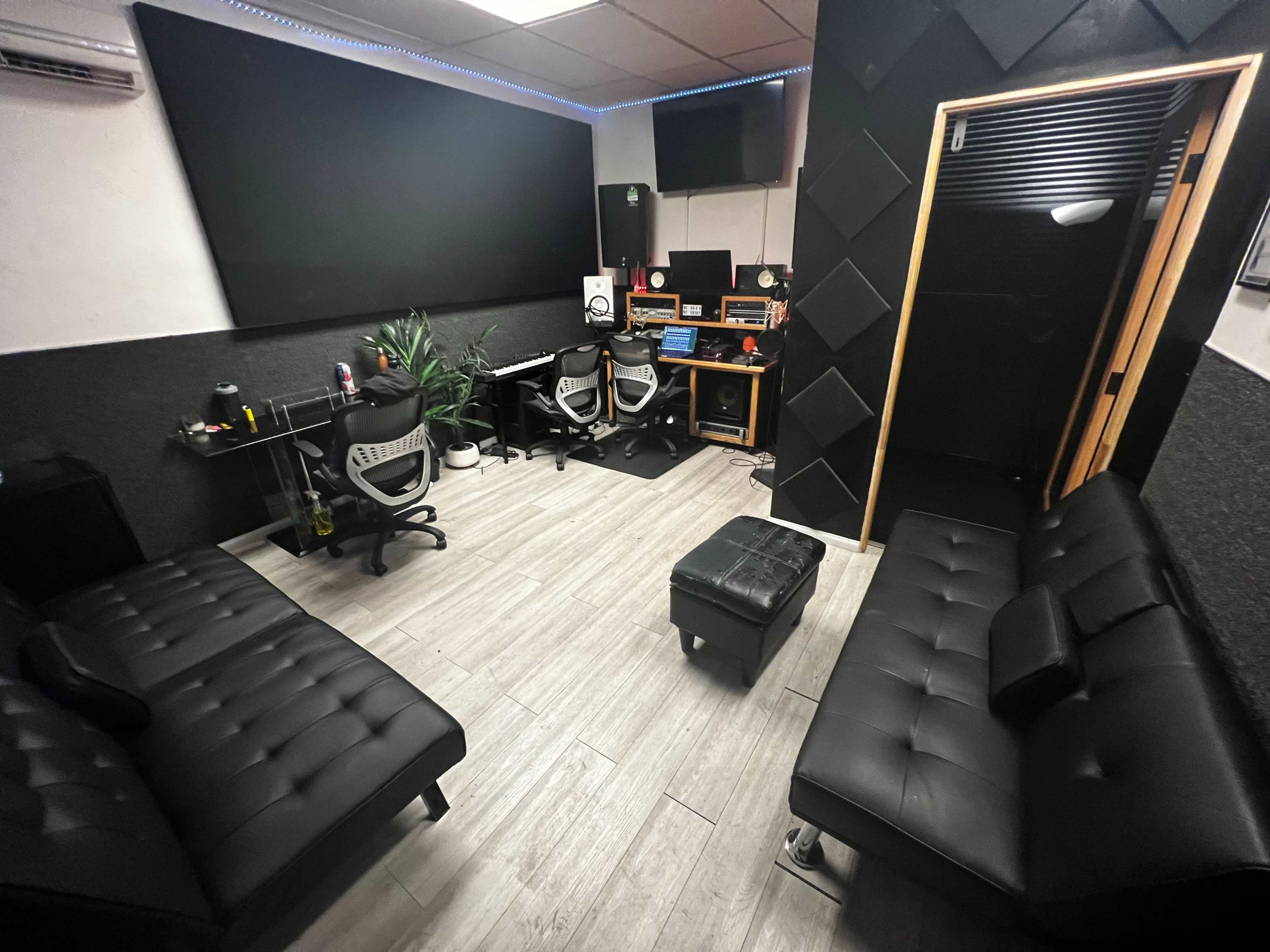 A recording studio with two black couches, a mixing desk, and sound equipment arranged in a sleek, minimalist layout.