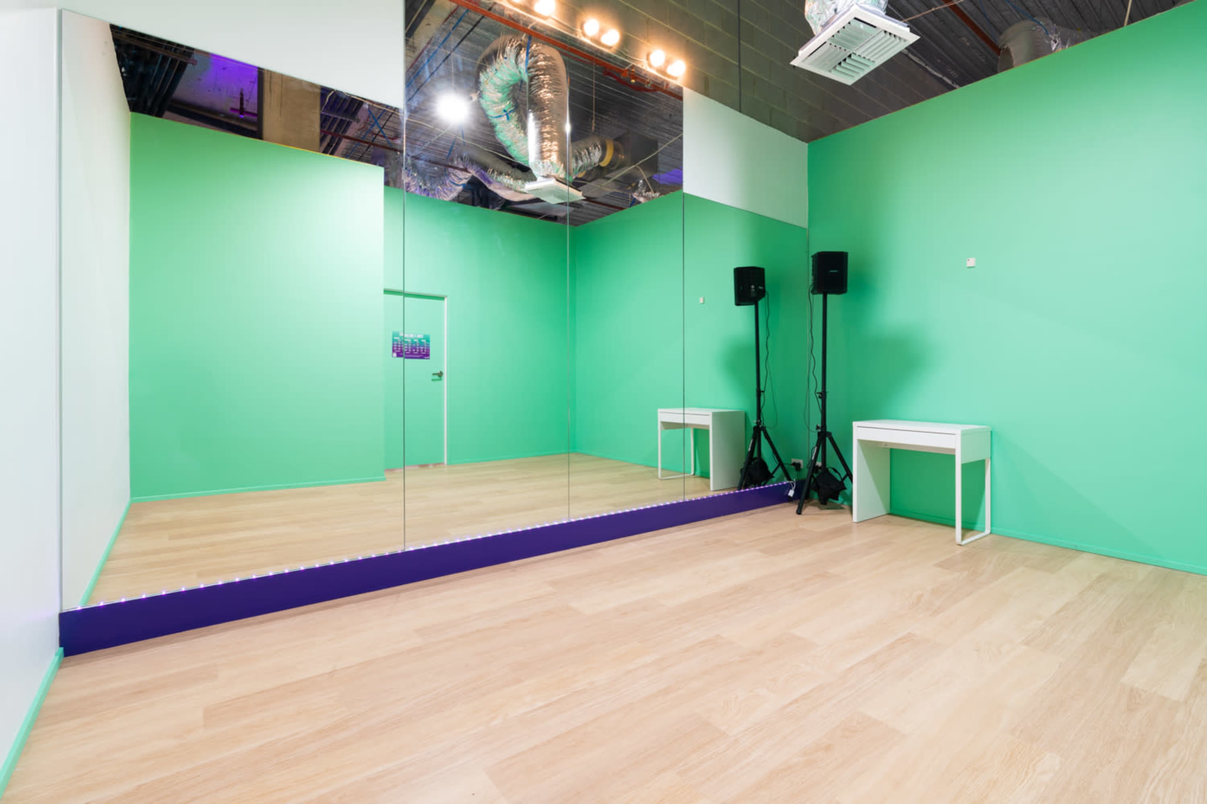 A bright green empty room with a large mirror on one wall, a small white table, and audio equipment in the corners.