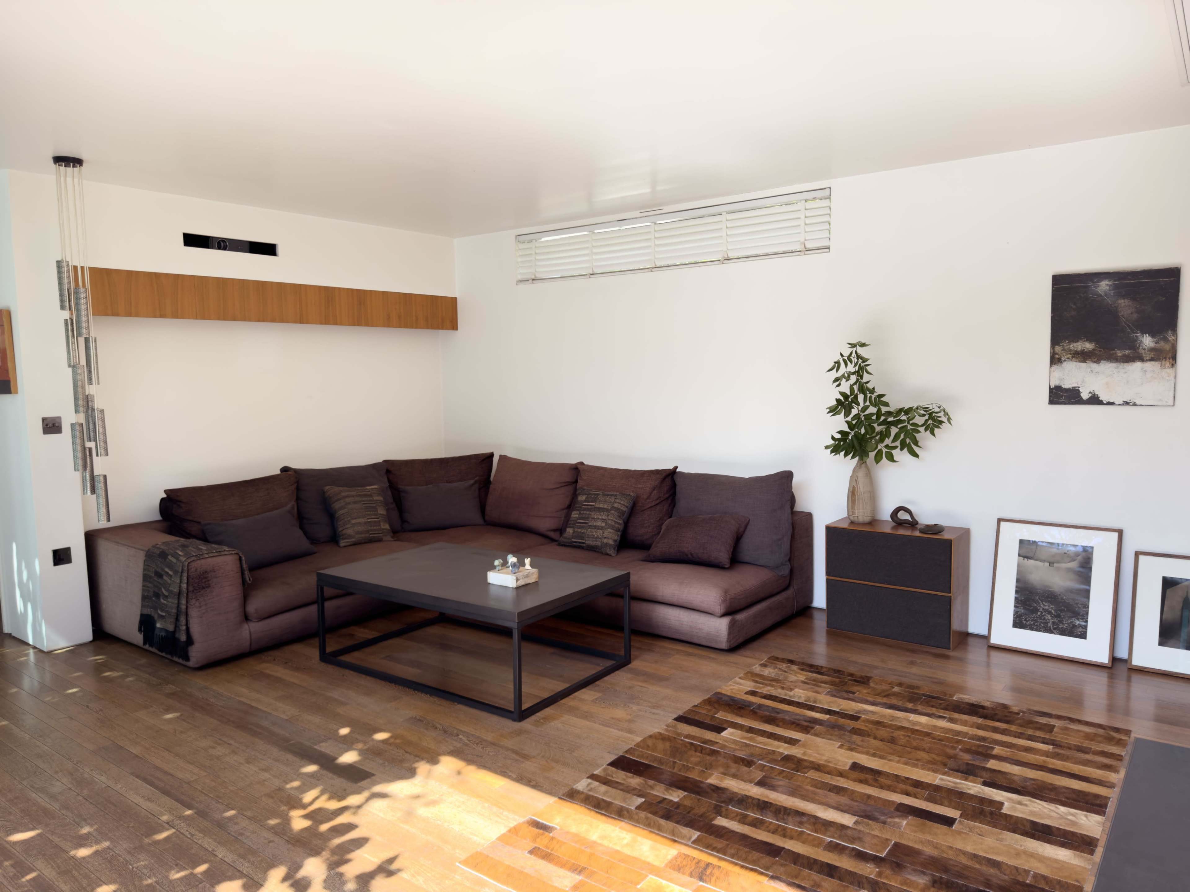 The image shows a modern living room featuring a large sectional sofa, a coffee table, and minimalistic decor against white walls and wooden flooring.