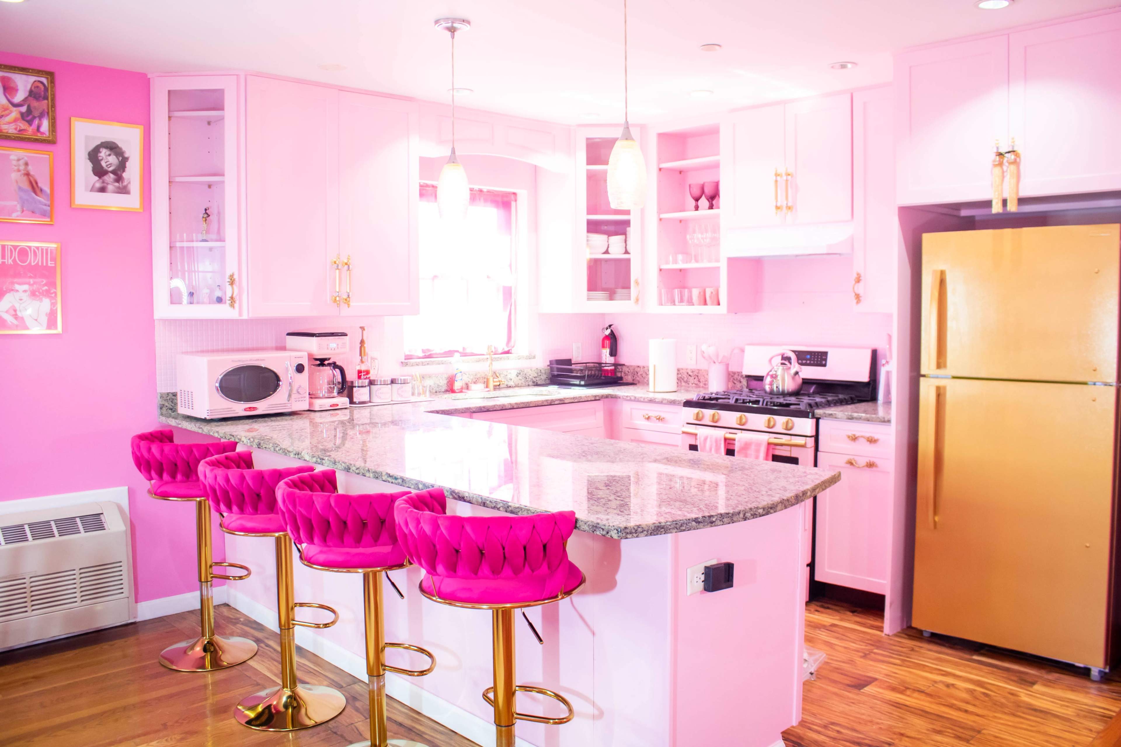 The image shows a stylish kitchen with pink walls, a pink granite island, and four pink barstools.