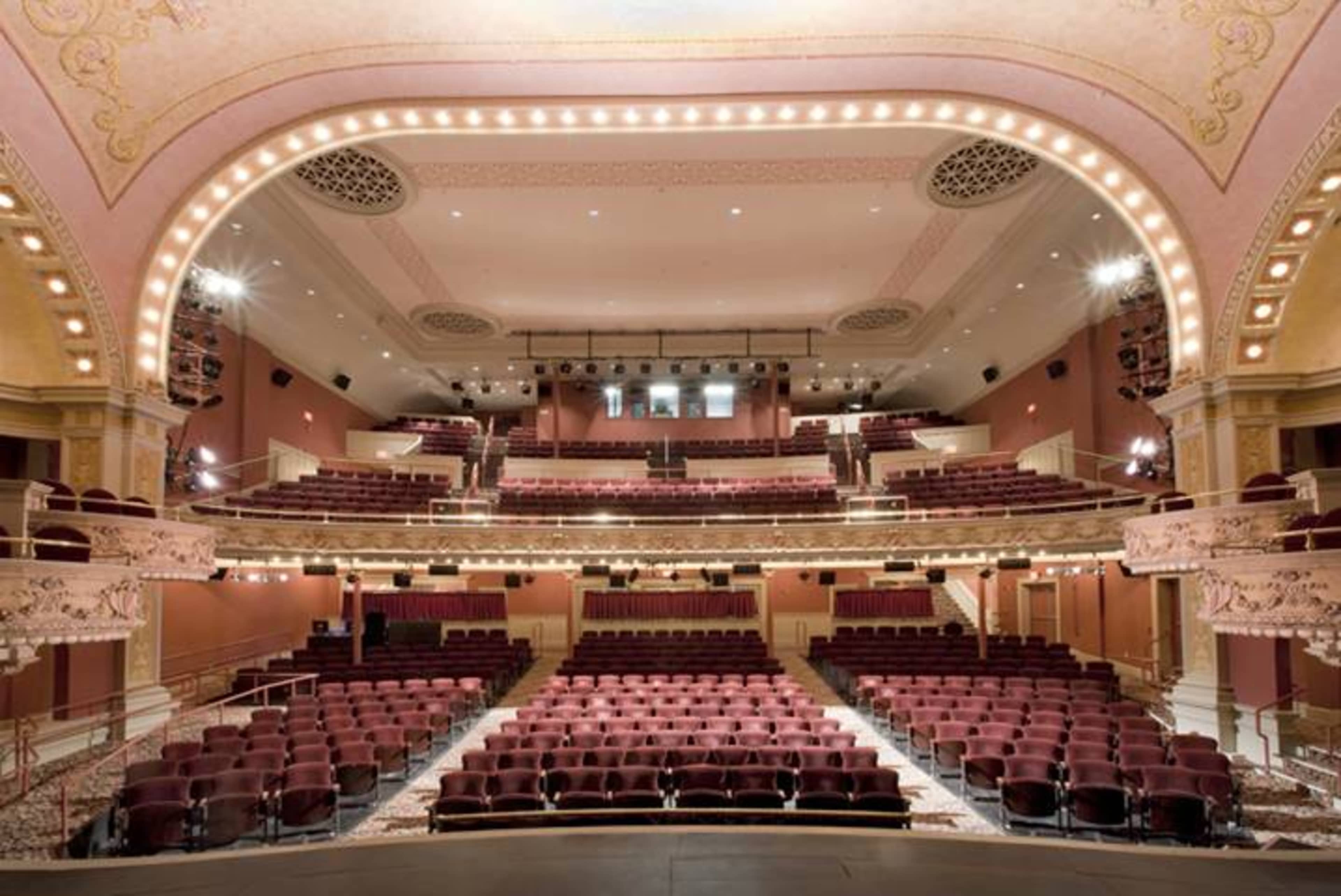 The interior of a theater featuring a grand stage, multiple levels of seating, and ornate architectural details.