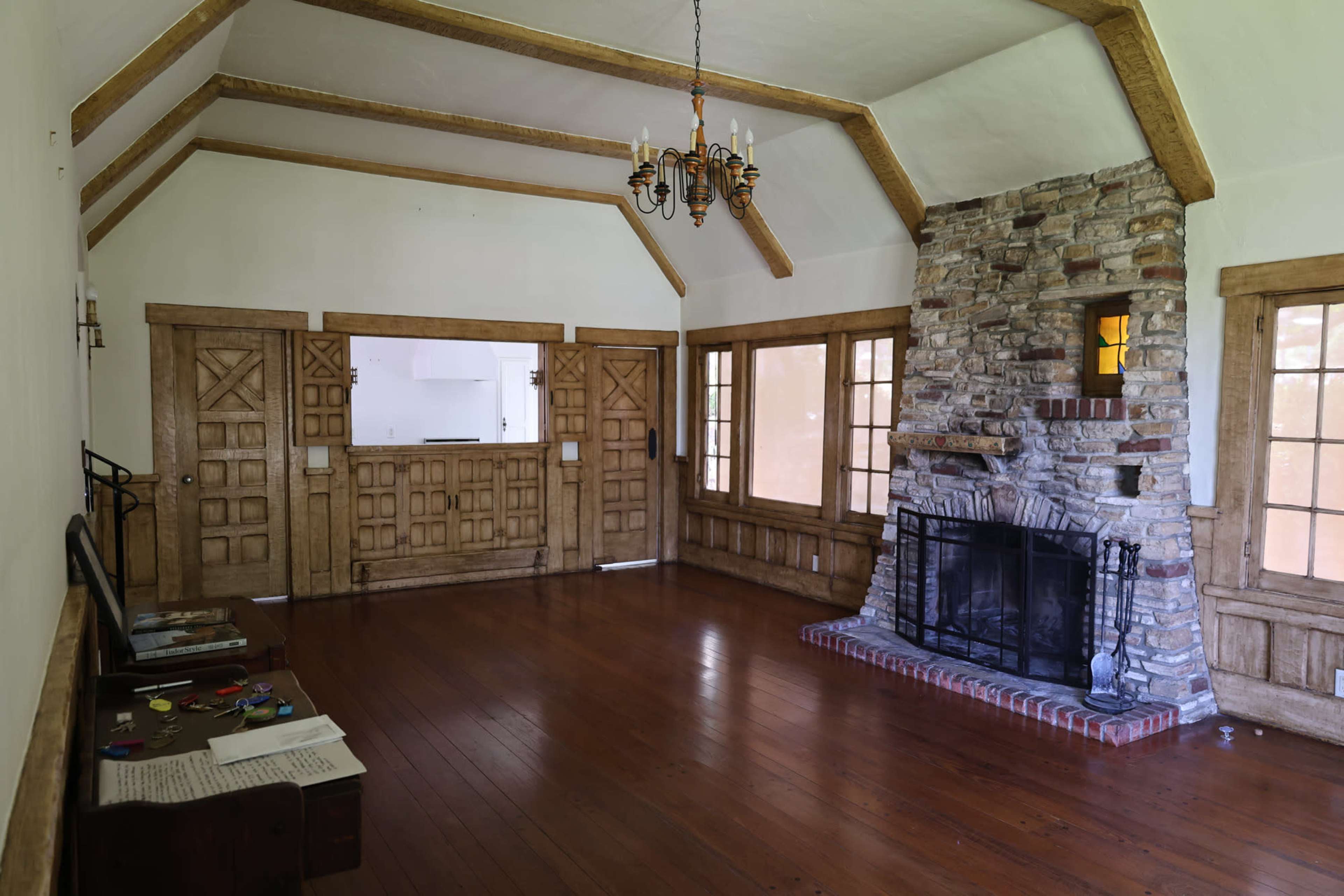 The image shows a spacious, empty room featuring a stone fireplace, wooden beams on the ceiling, and wooden doors along the walls.