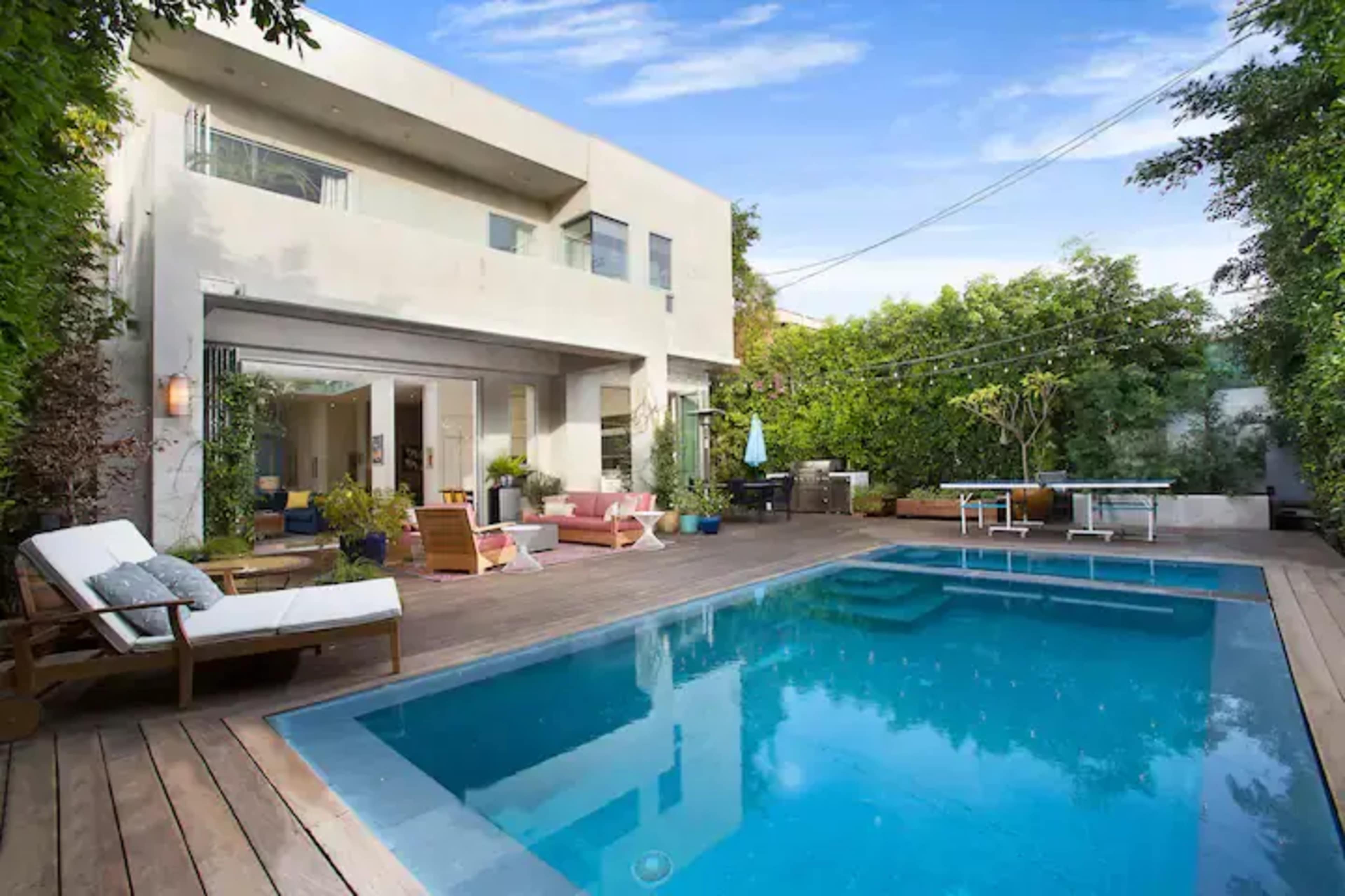 A modern house with a swimming pool is surrounded by lush greenery and outdoor seating areas.