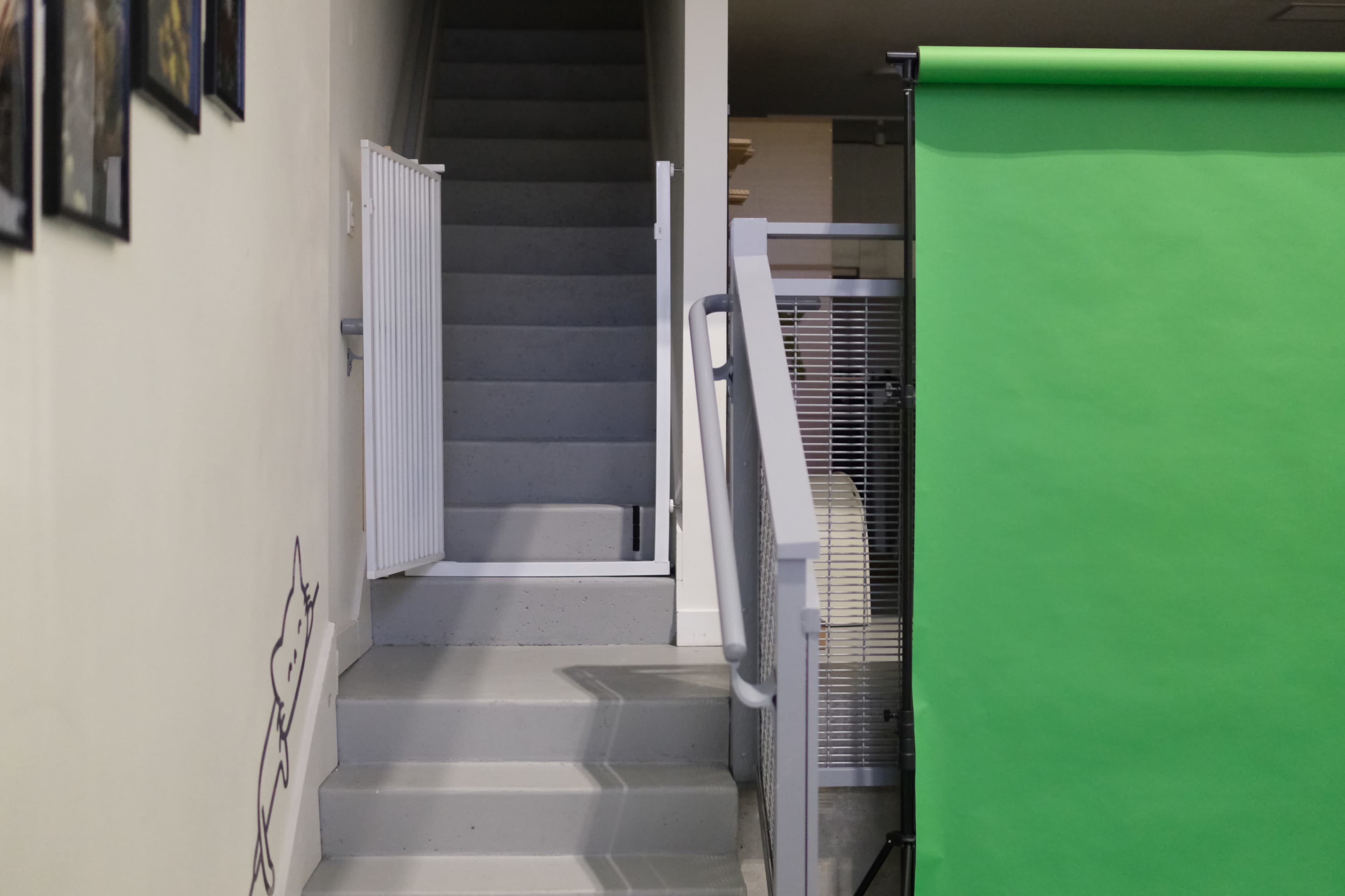 A staircase leads upward to a landing beside a green screen and a wall with framed pictures.