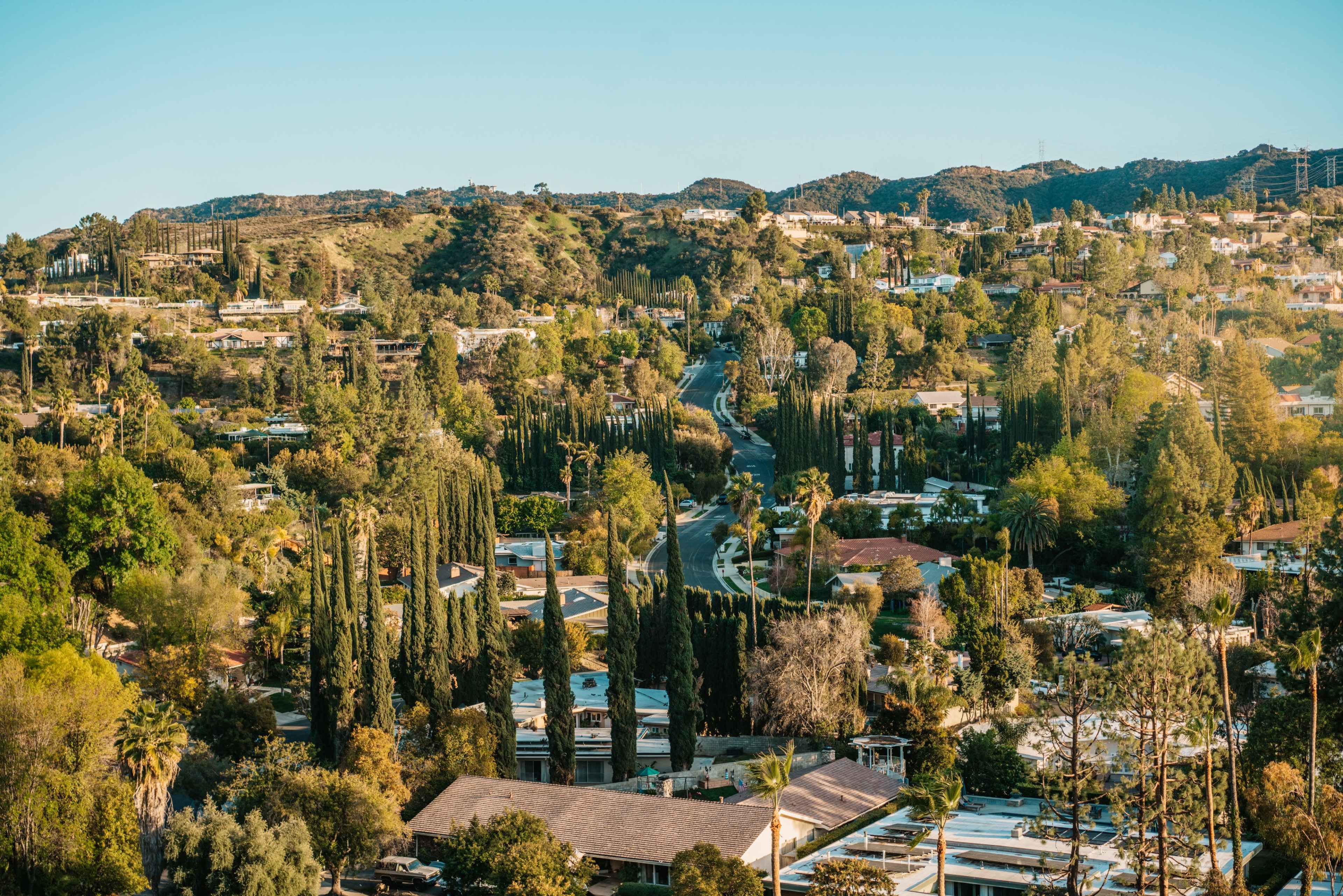 A hilly residential area with winding roads, houses, and dense trees.