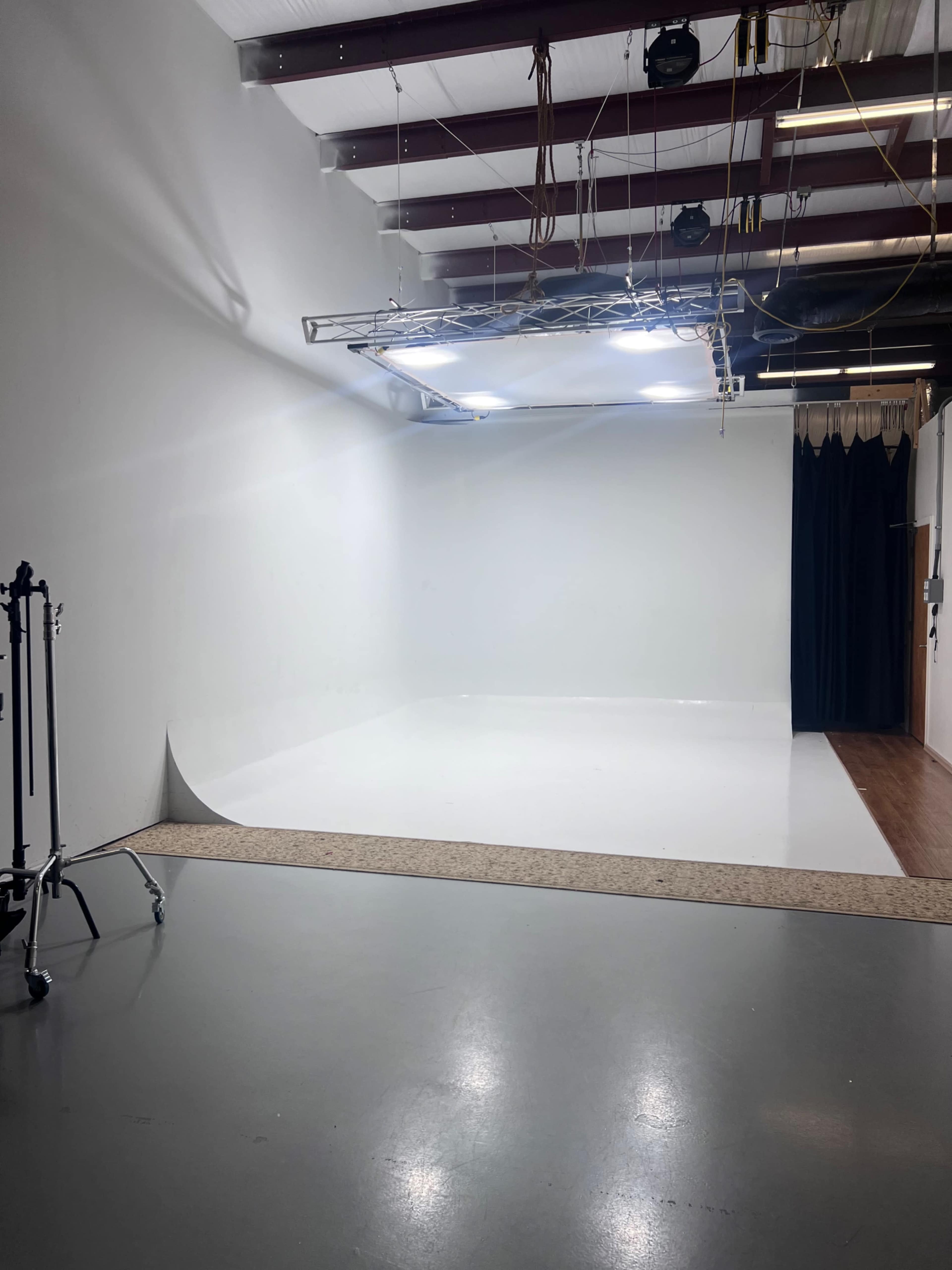 A blank photography studio with a white backdrop, a lighting setup above, and a dark curtain on one side.