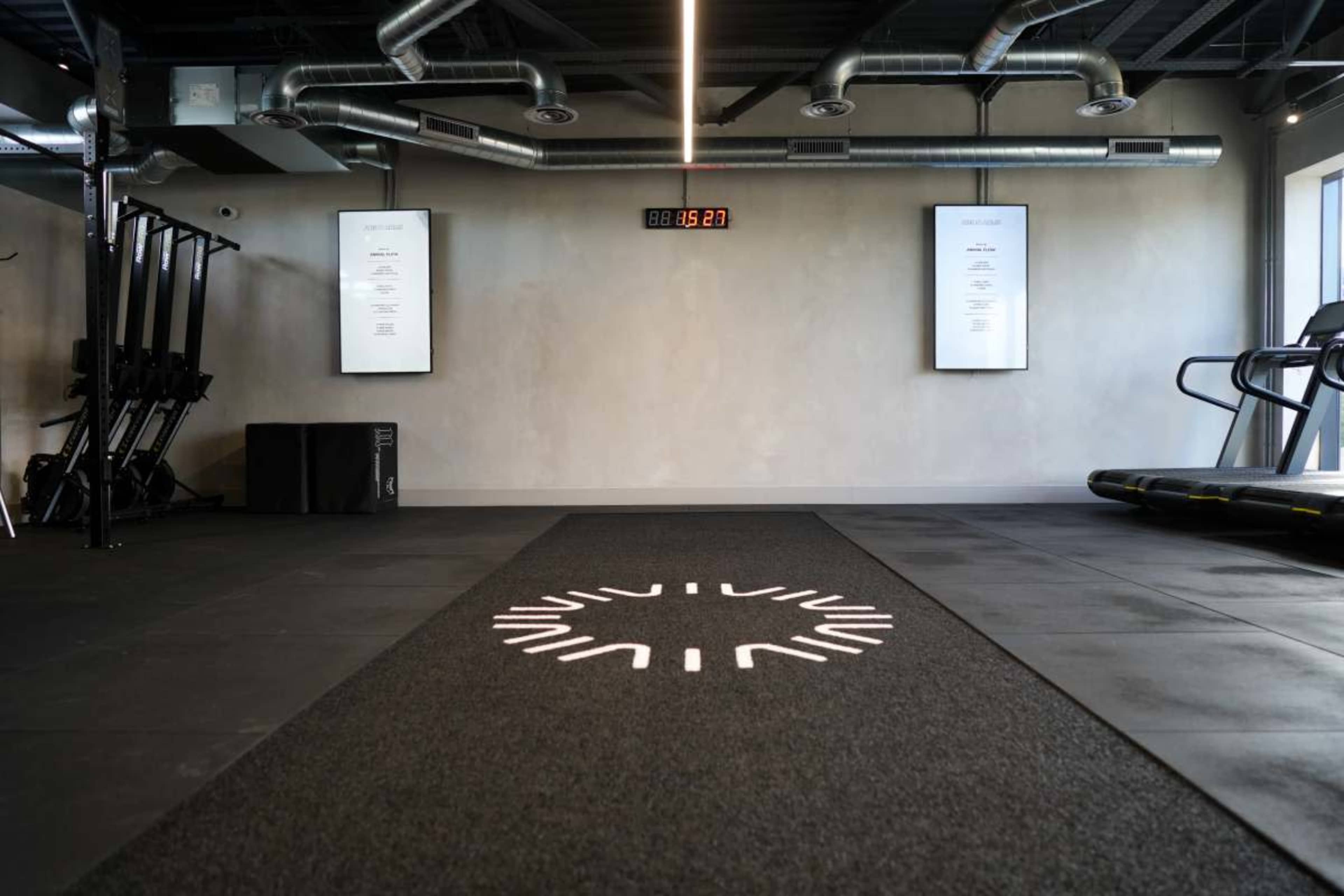 The image shows a modern gym interior featuring a black workout mat with a circular design, treadmill, and exercise equipment.