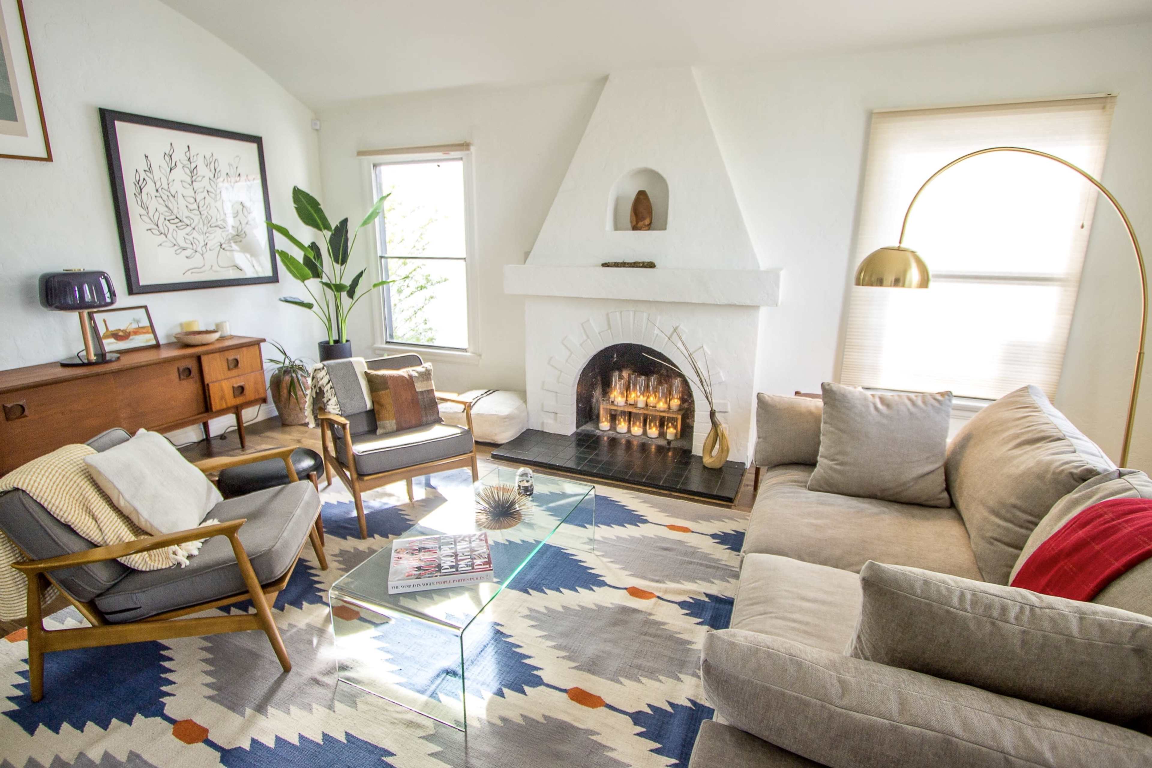 A modern living room featuring a fireplace, a large sofa, stylish chairs, and a geometric area rug.