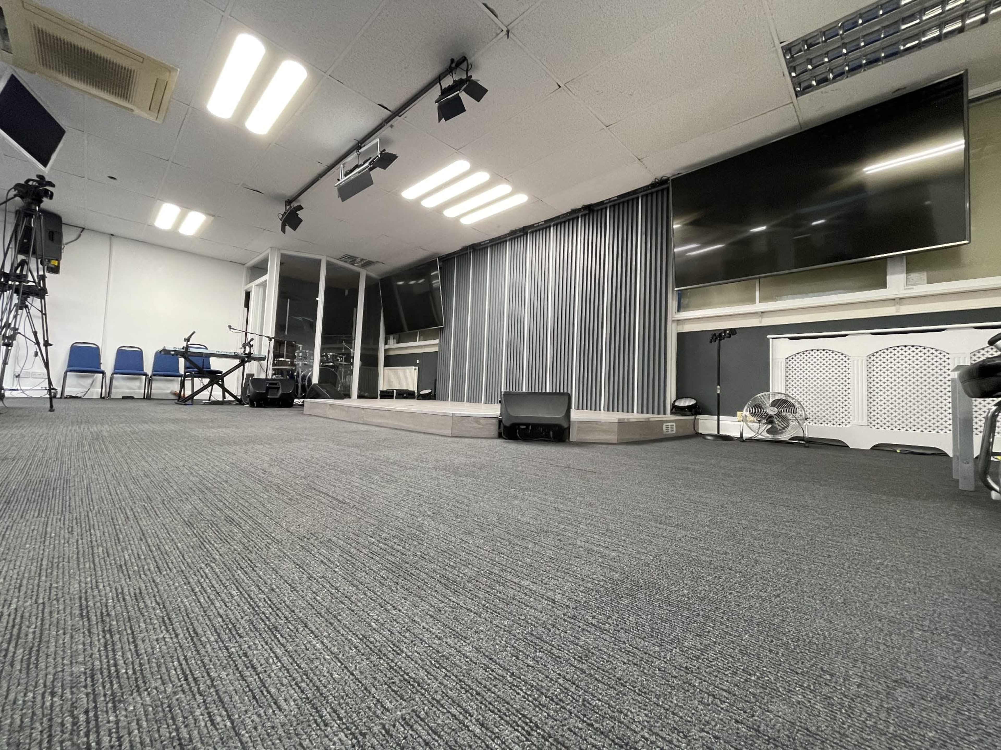 An empty room designed for presentations, featuring a stage with curtains, several television screens, and a sound system.