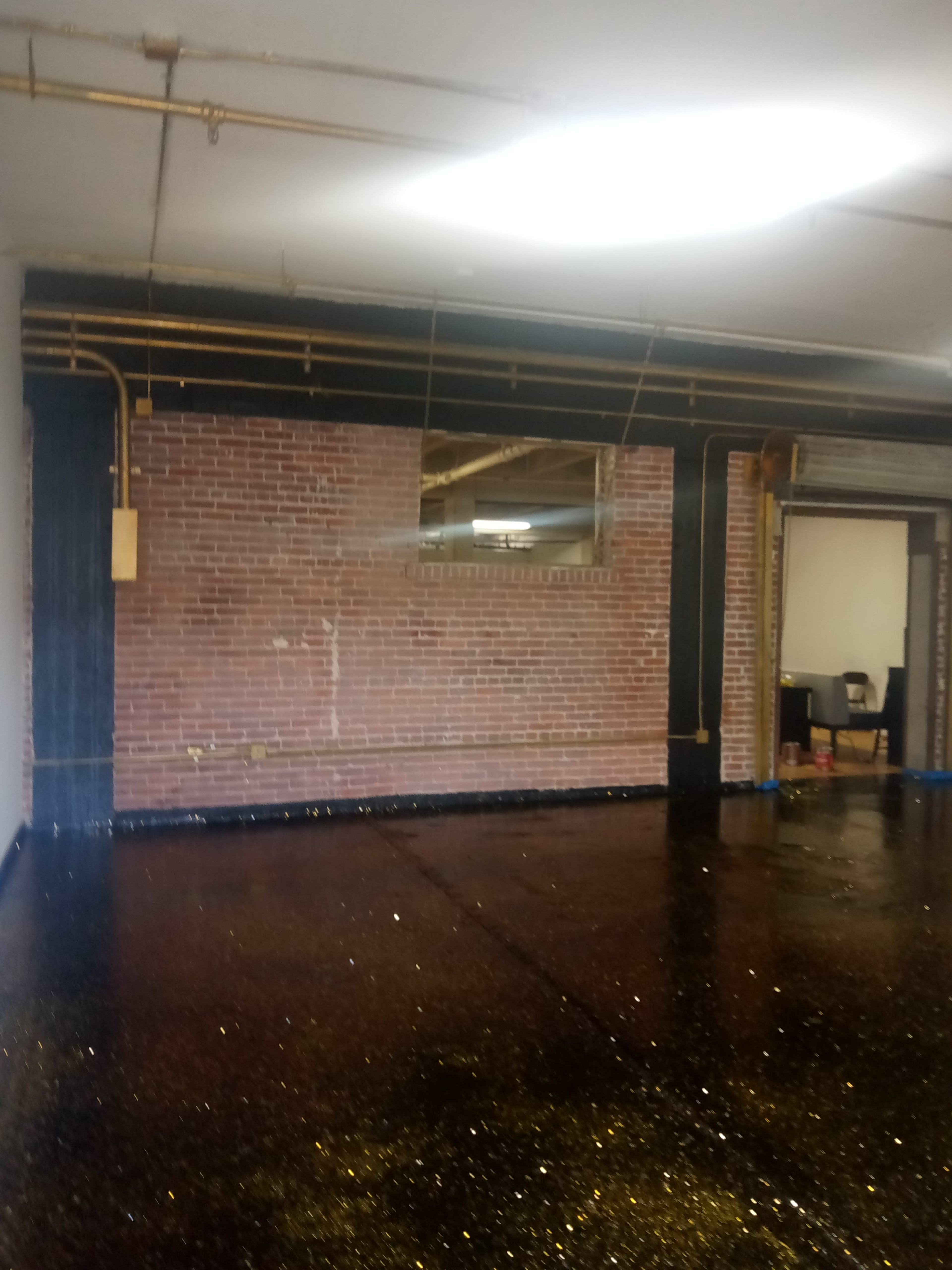 A spacious industrial-style room with a brick wall, a mirror, and a glossy black floor speckled with gold glitter.