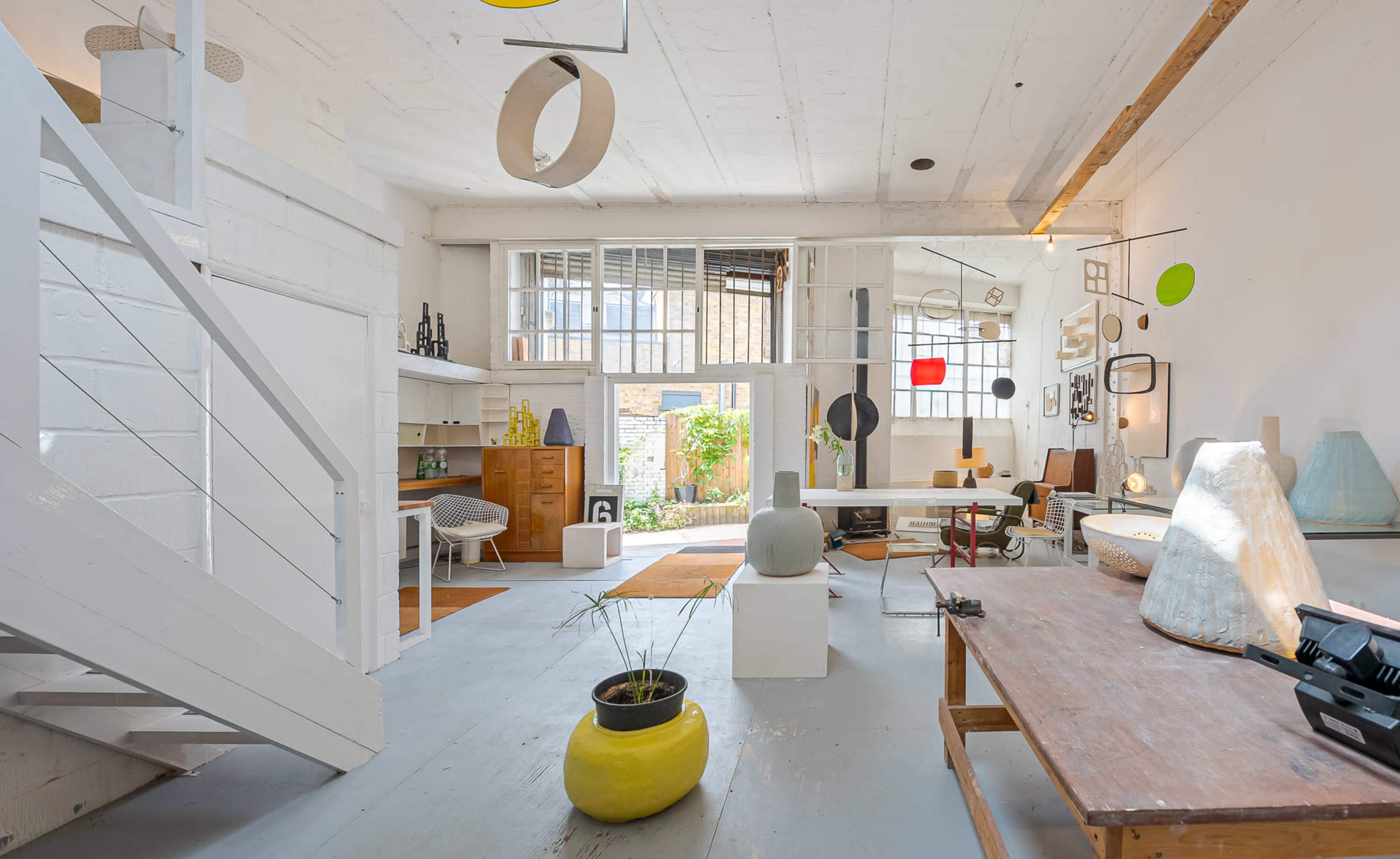 The image shows a spacious, modern interior with white walls, various decorative objects, and a view of a garden through large windows.