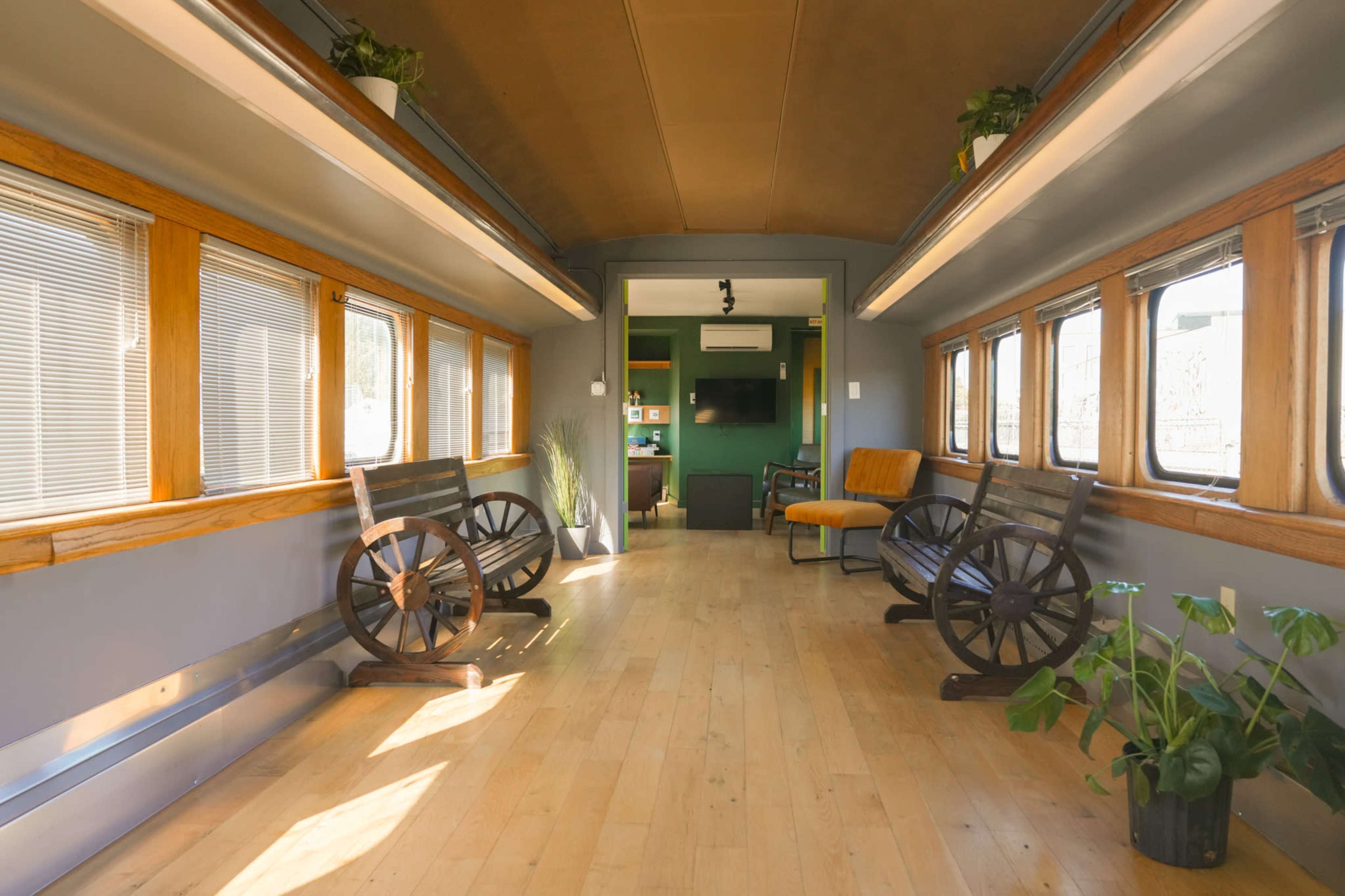 The interior of a converted train car features wooden flooring, large windows, and seating areas with decorative wheels along the walls.