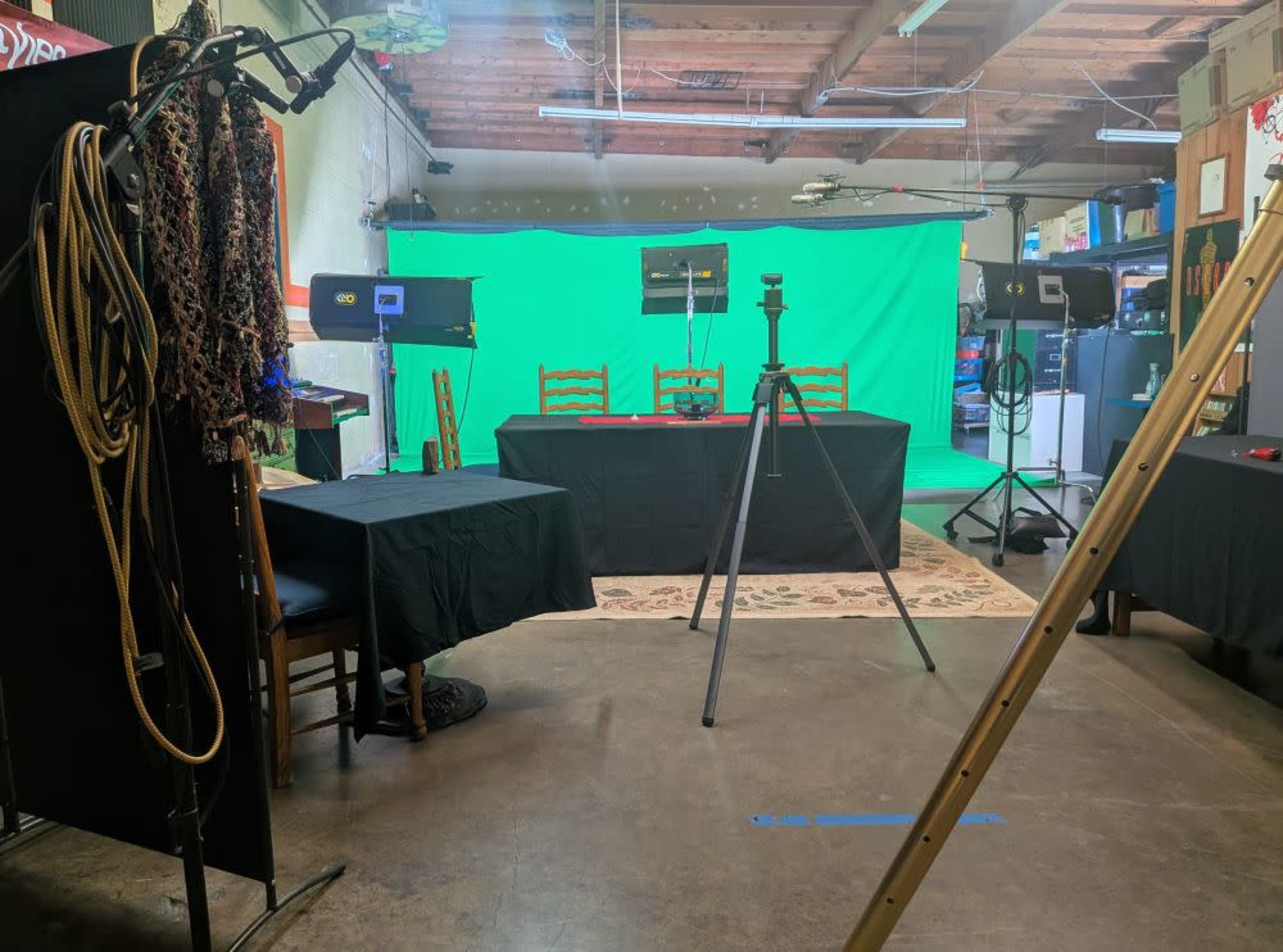 The image shows a studio setup with a green screen, two chairs, tripods, and various lighting equipment arranged in a spacious room.