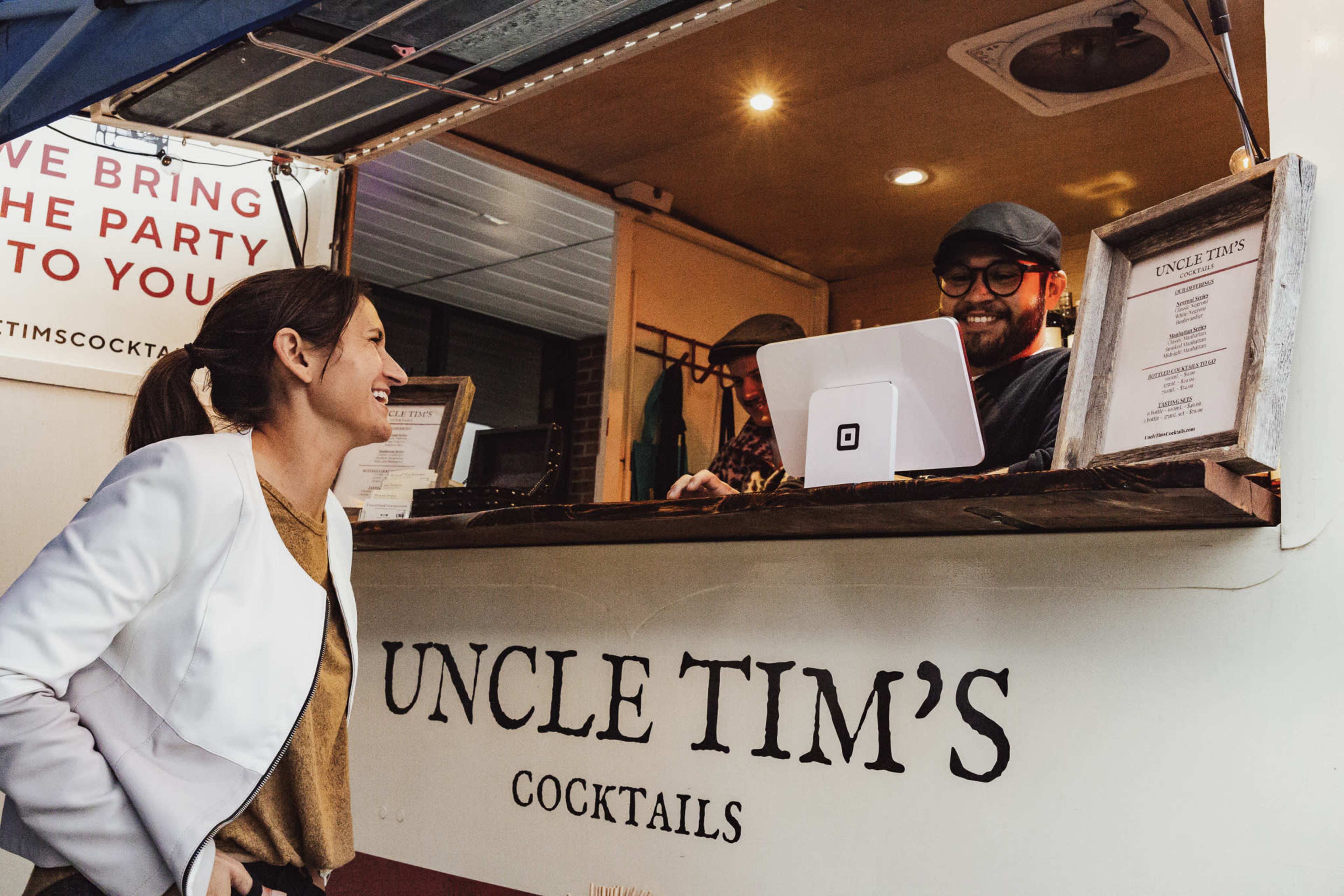A woman smiles while interacting with a bartender inside a cocktail food truck.