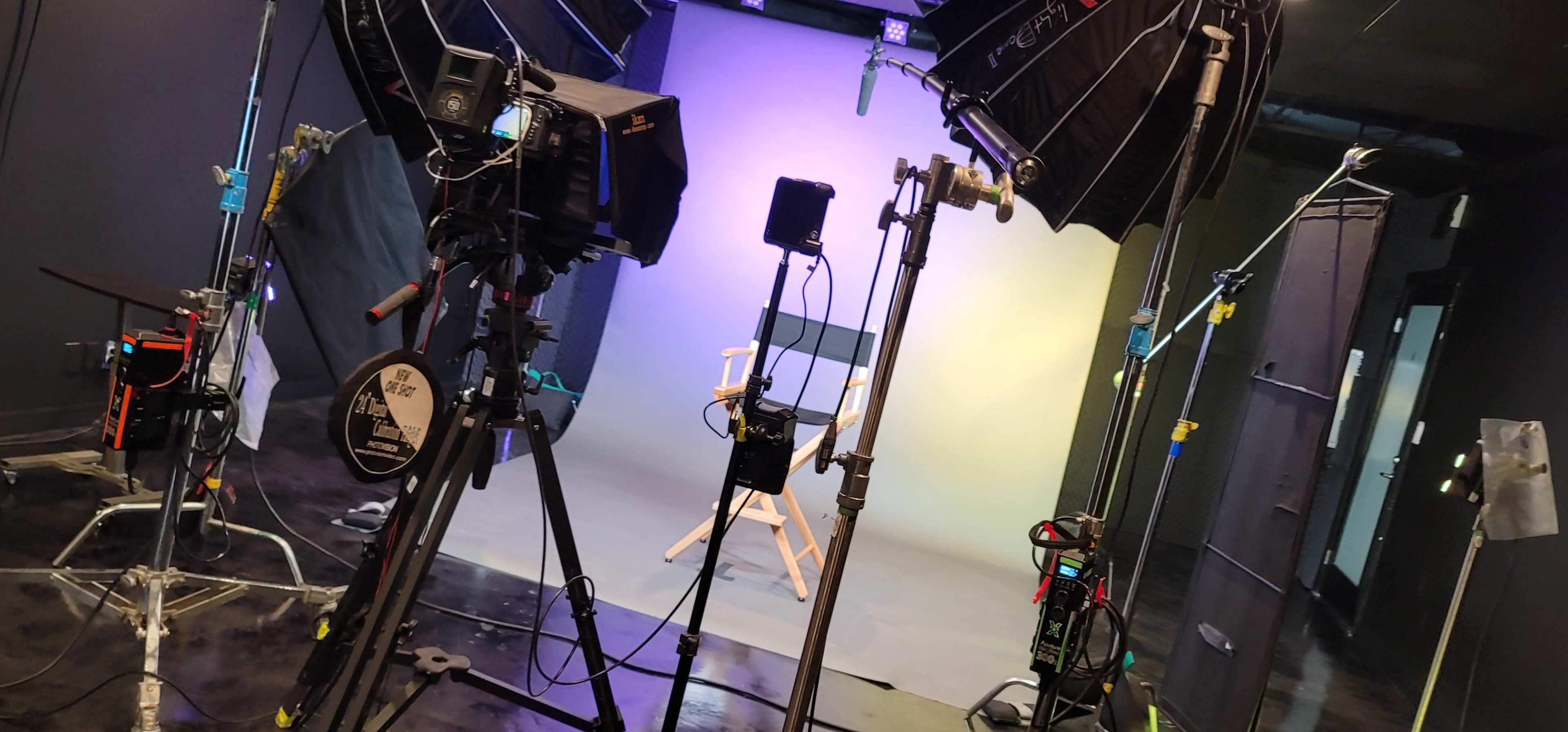 A video recording studio set up with multiple cameras, lights, and a director's chair against a gradient backdrop.