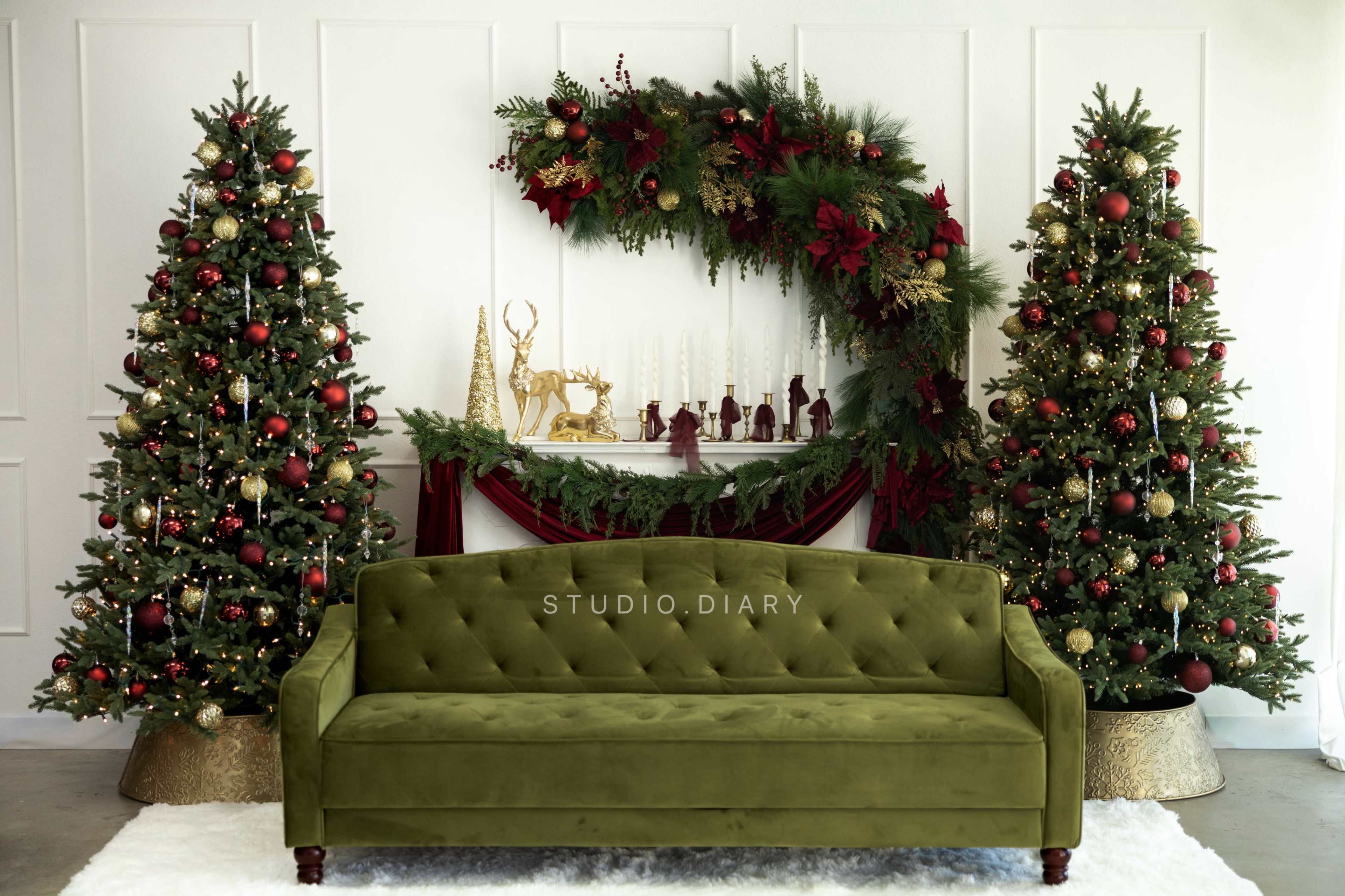 The image features a green velvet sofa centered between two decorated Christmas trees, with a festive backdrop of a mantel adorned with holiday decorations.