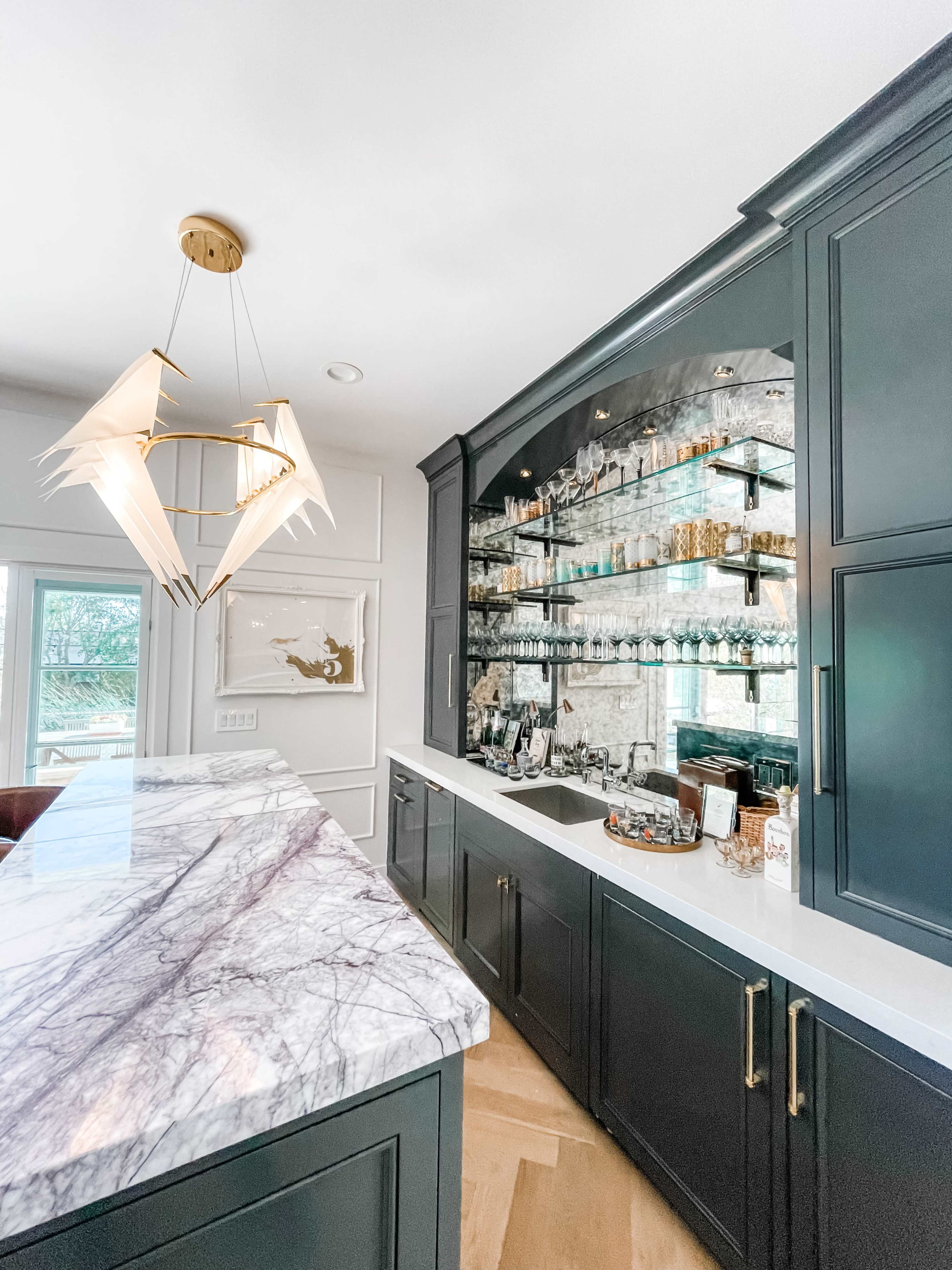 A modern kitchen features dark cabinetry, a marble countertop, and a glass-fronted cabinet displaying various glassware and decorative items.