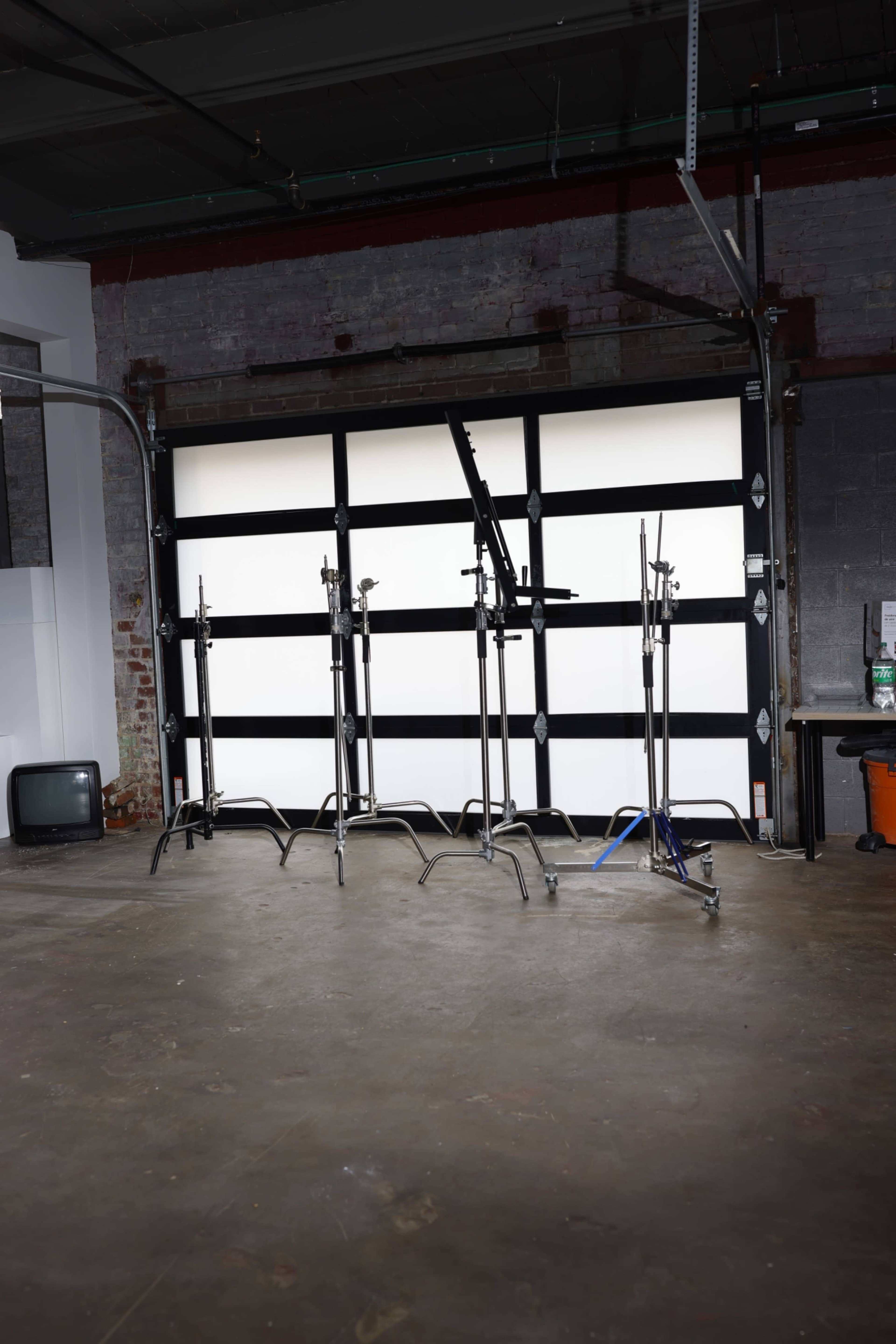 The image shows a series of metal clothing racks lined up in front of a large, white garage door set against a concrete floor.