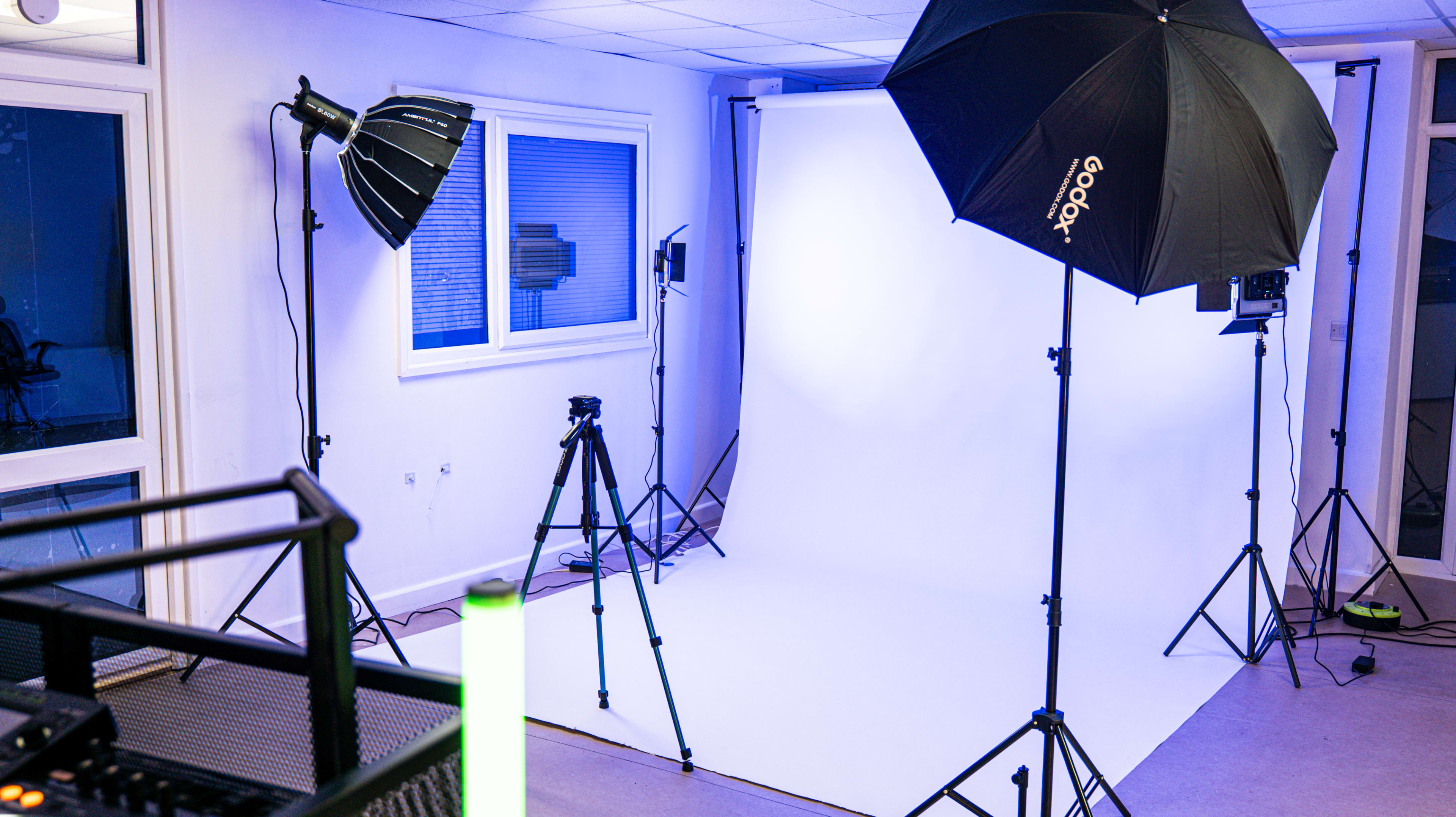 The image shows a photography studio equipped with various lighting setups, tripods, and a white backdrop.