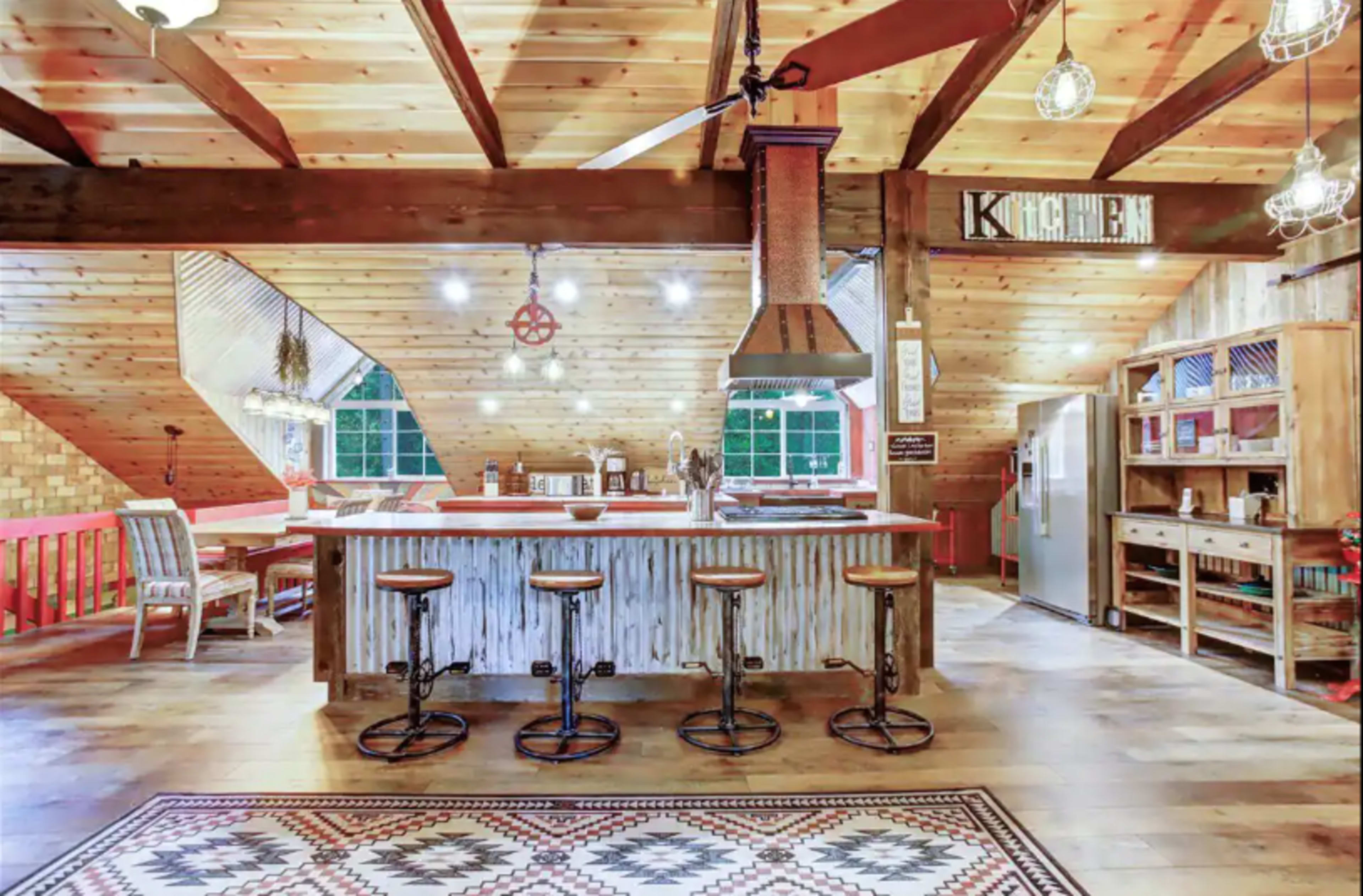 A spacious, rustic kitchen with wooden beams, a large island with metal accents, and three bar stools.