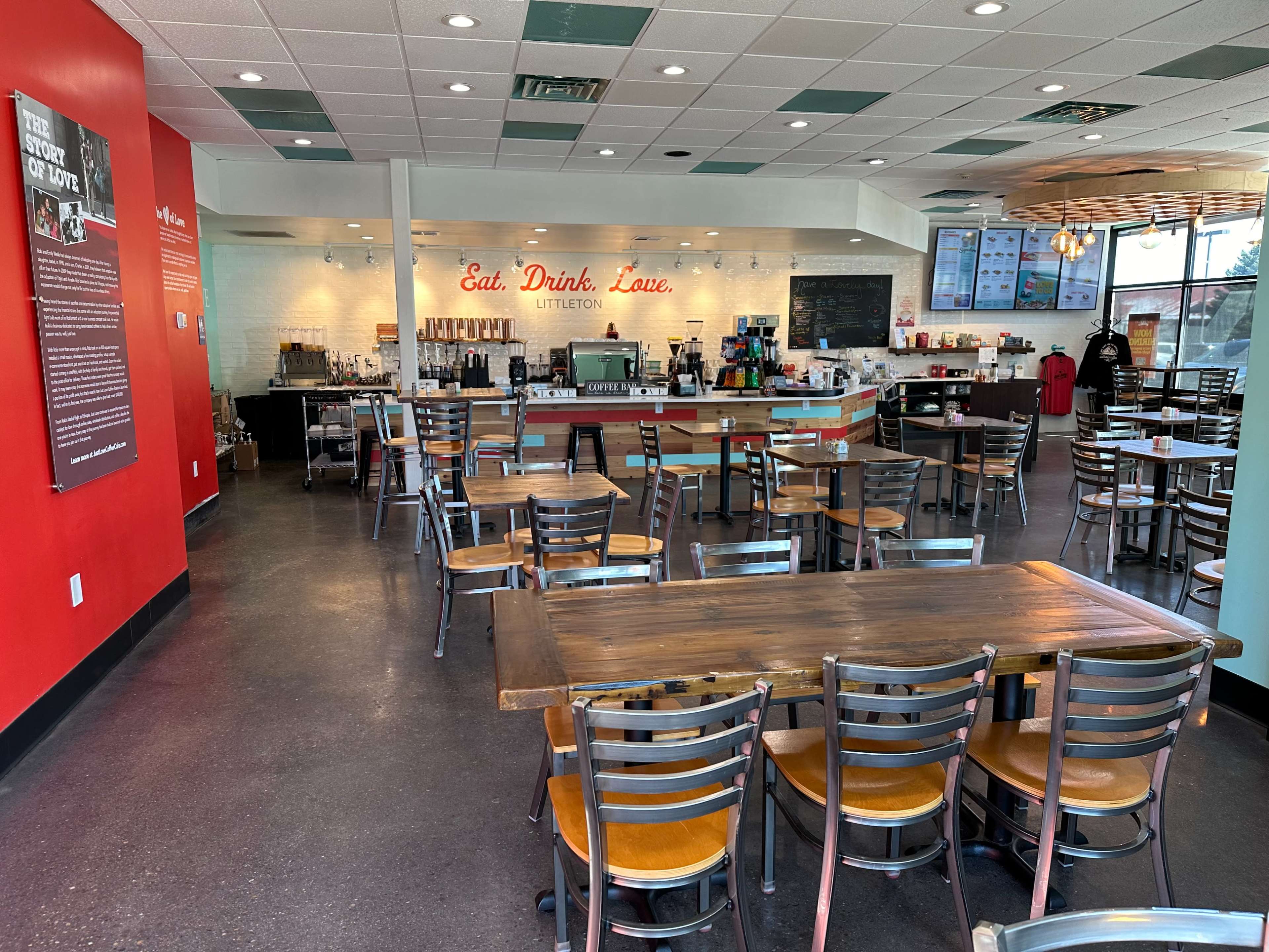 The interior of a casual dining restaurant with a combination of wooden tables and metal chairs, a counter area with beverage stations, and red accent walls.