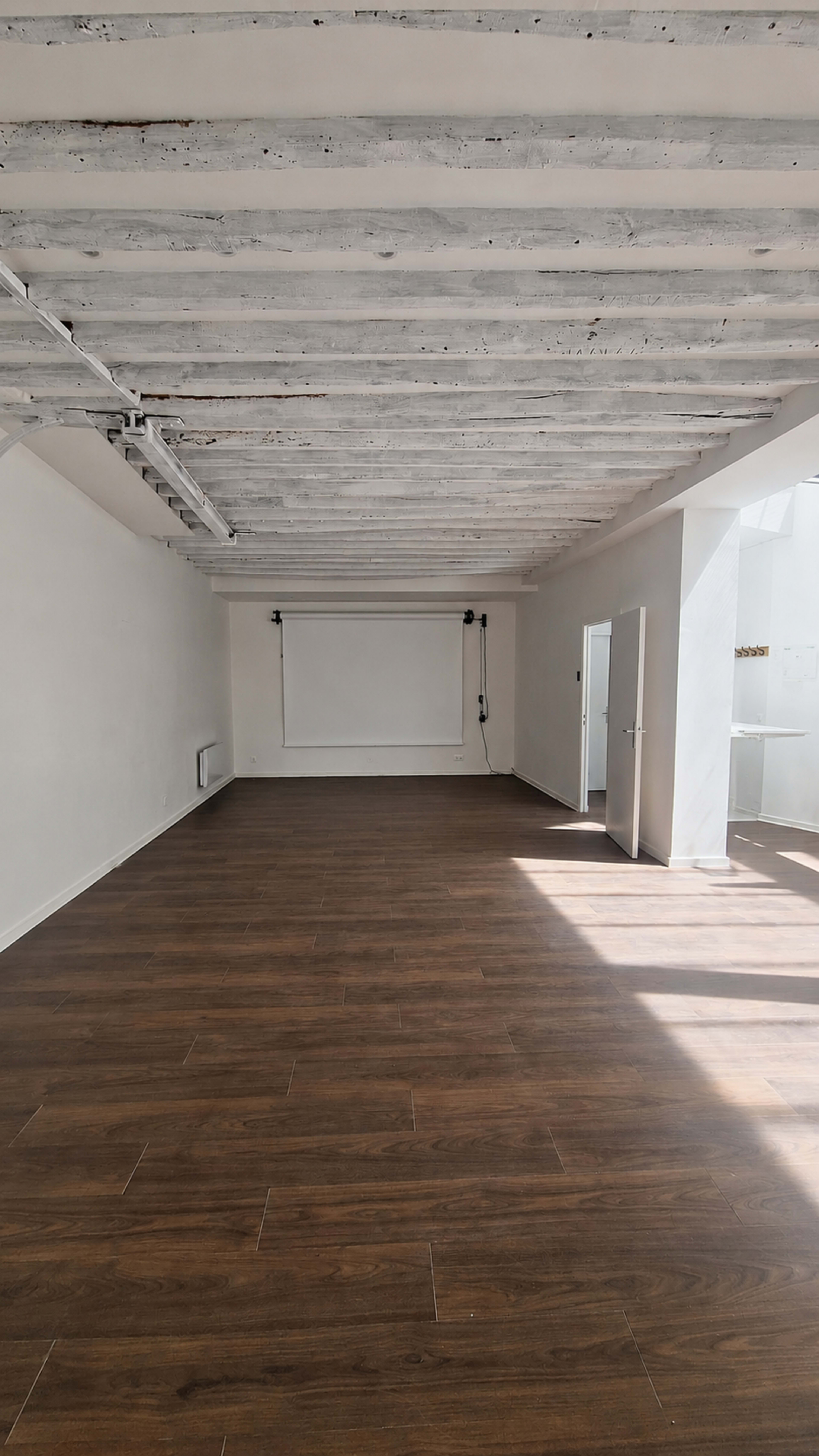 The image shows an empty room with wooden flooring, white walls, and exposed wooden ceiling beams.